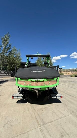 A green 2018 Nautique Super Air Nautique G23 boat on a trailer in a parking area.