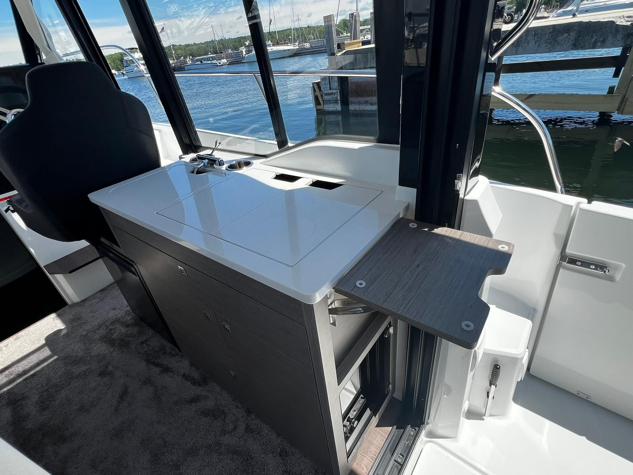 Interior of 2025 Jeanneau NC 895 boat with compact kitchen and water view.