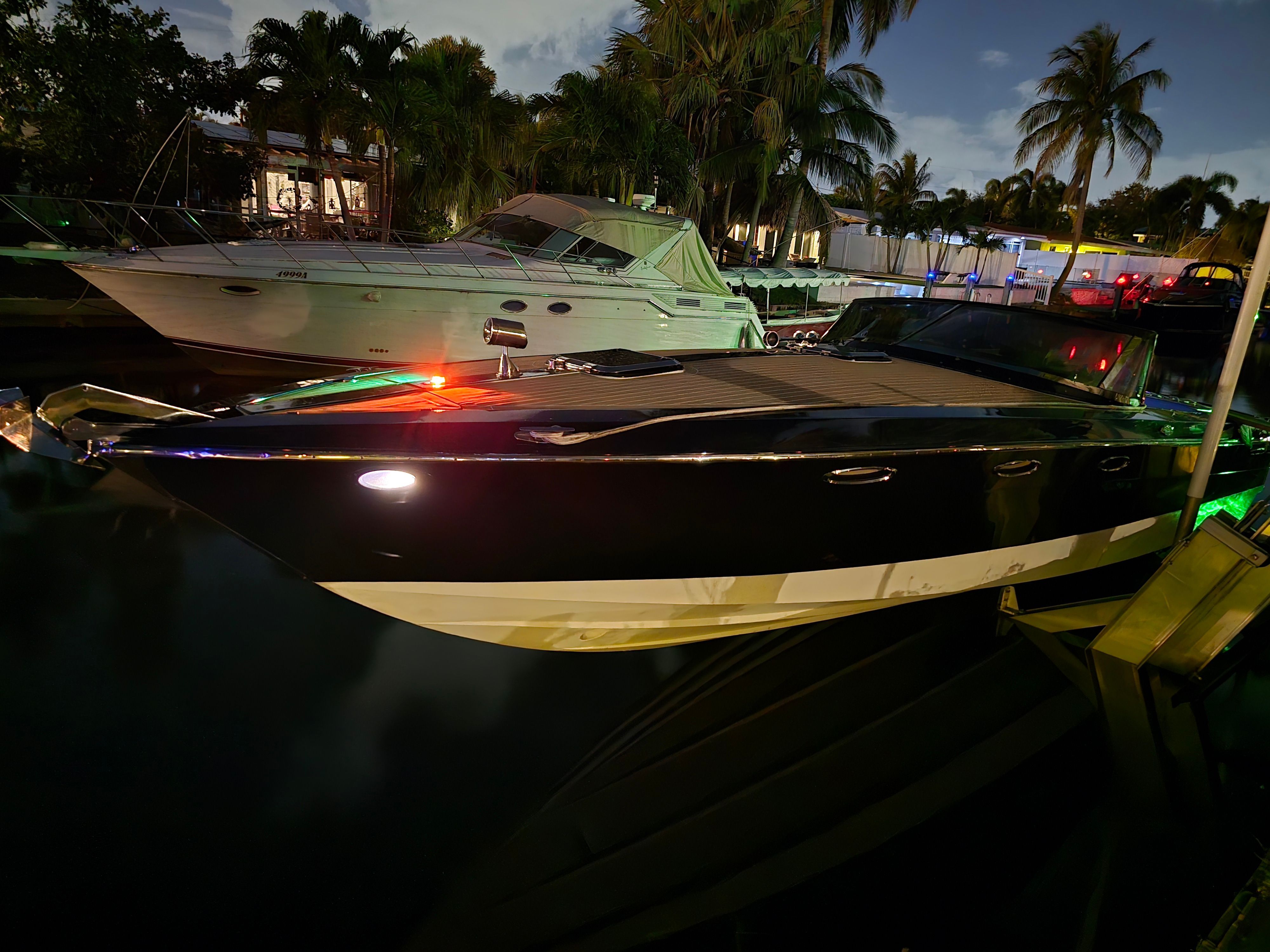 A sleek motorboat is docked at night, surrounded by palm trees and other boats.