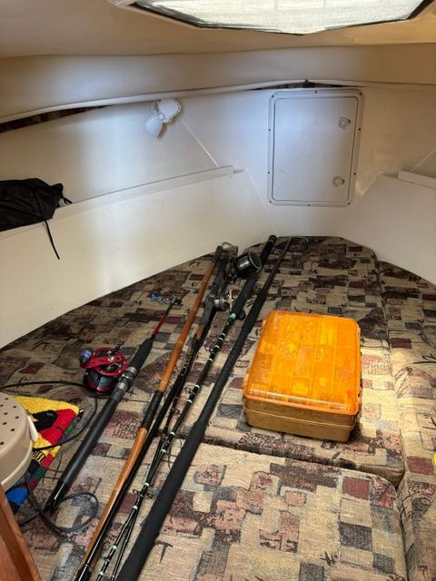 Interior of a boat with fishing rods and an orange box on a patterned seat.