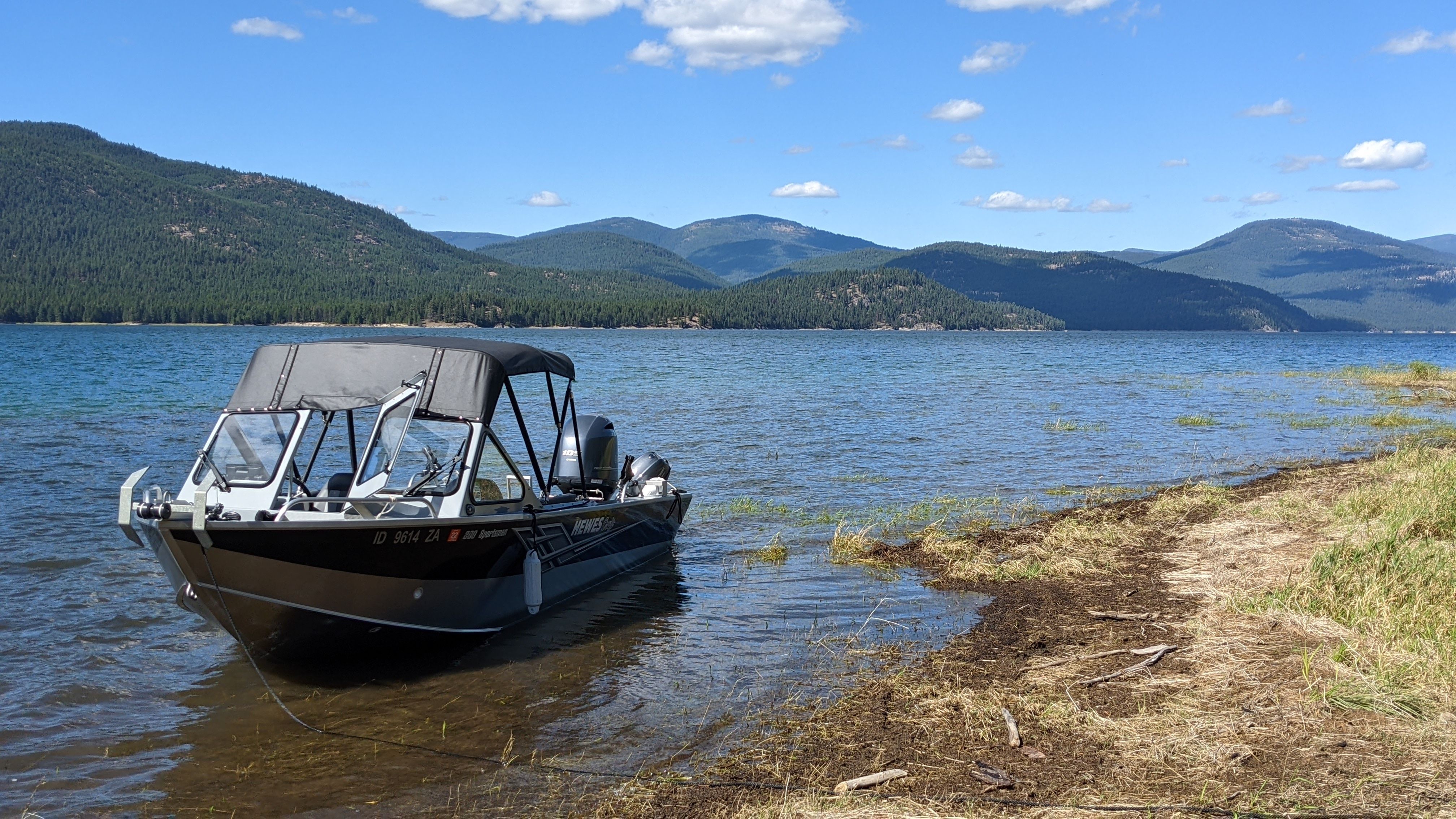 A 2020 Hewescraft 200 Sportsman is moored by a calm lake shore with mountain views.