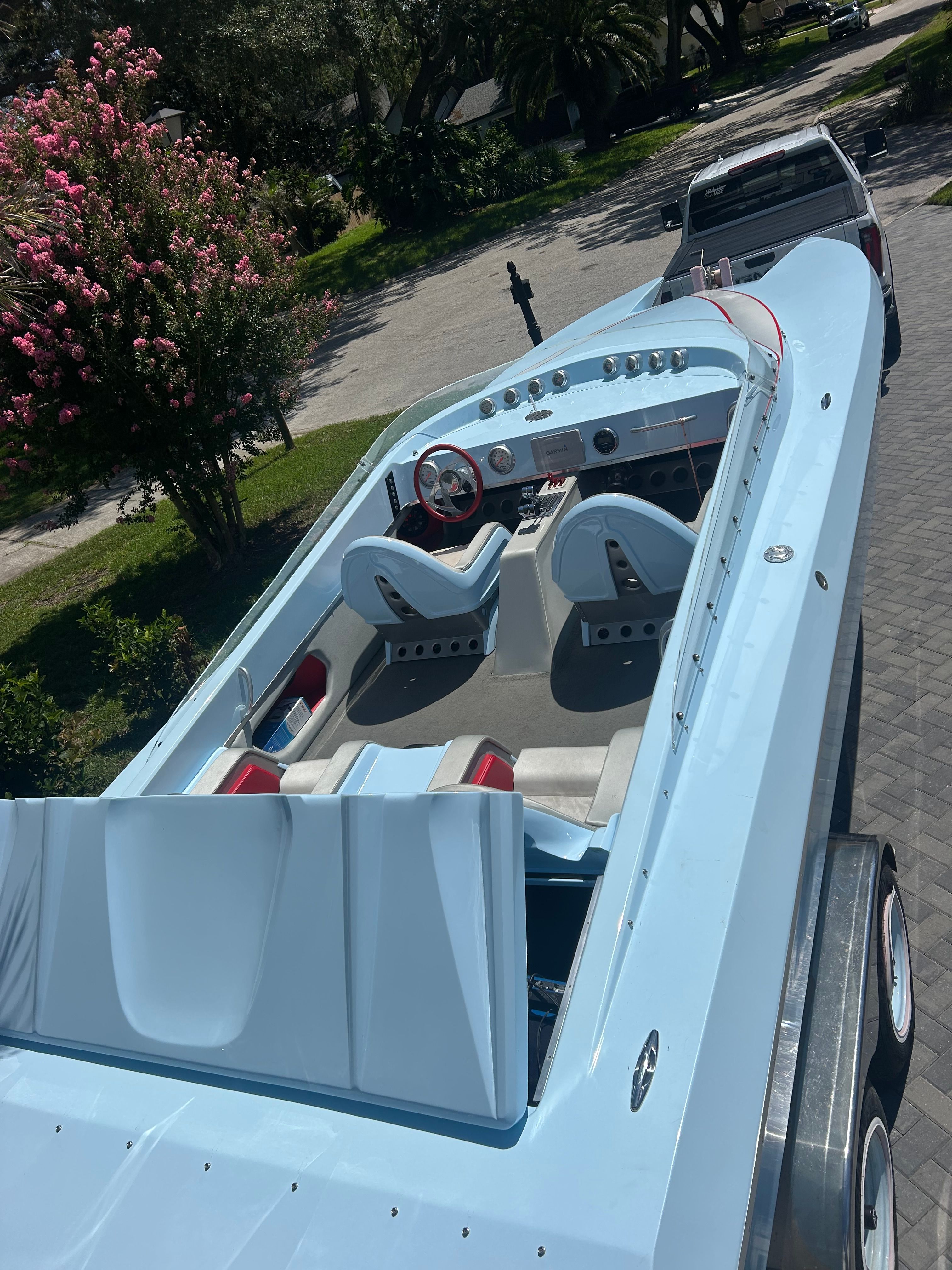 A light blue motorboat with two seats and a red steering wheel on a trailer.