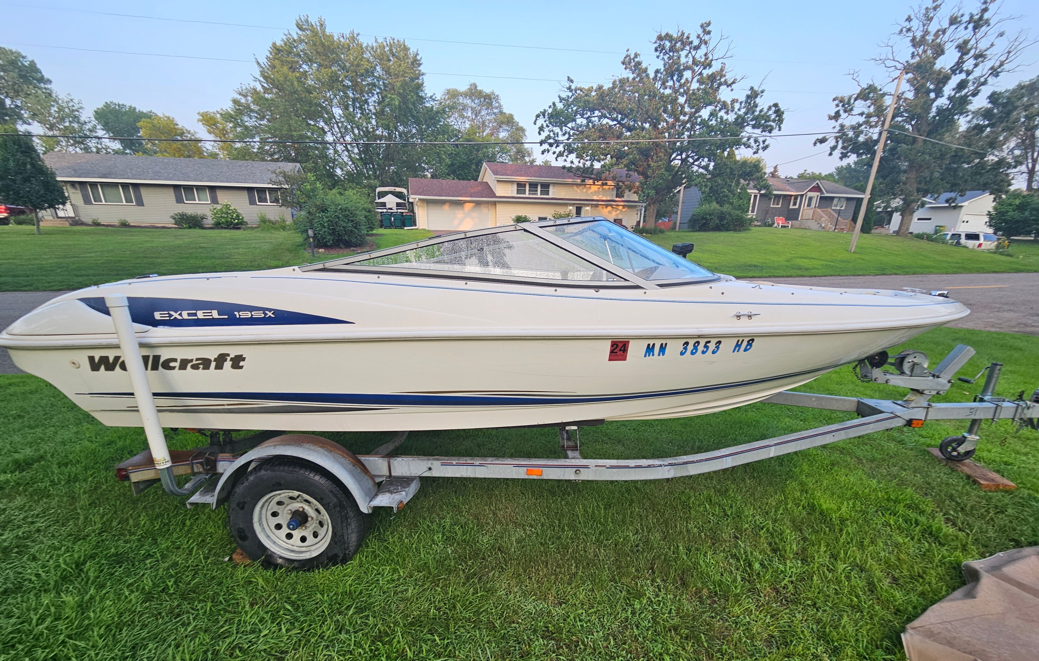 A 1996 Wellcraft Excel boat on a trailer, parked on a lawn.
