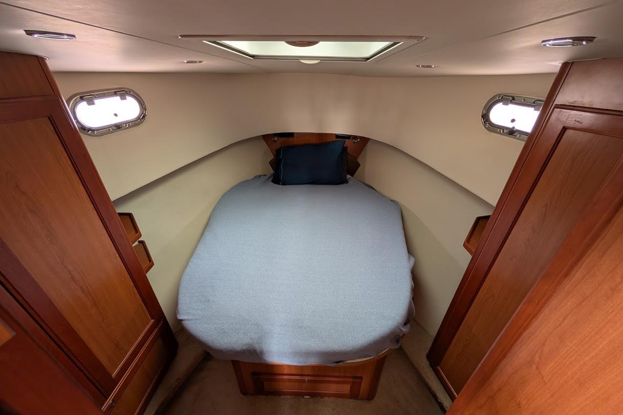 Cozy cabin interior of 2008 Mainship 38 with bed and wooden cabinetry.