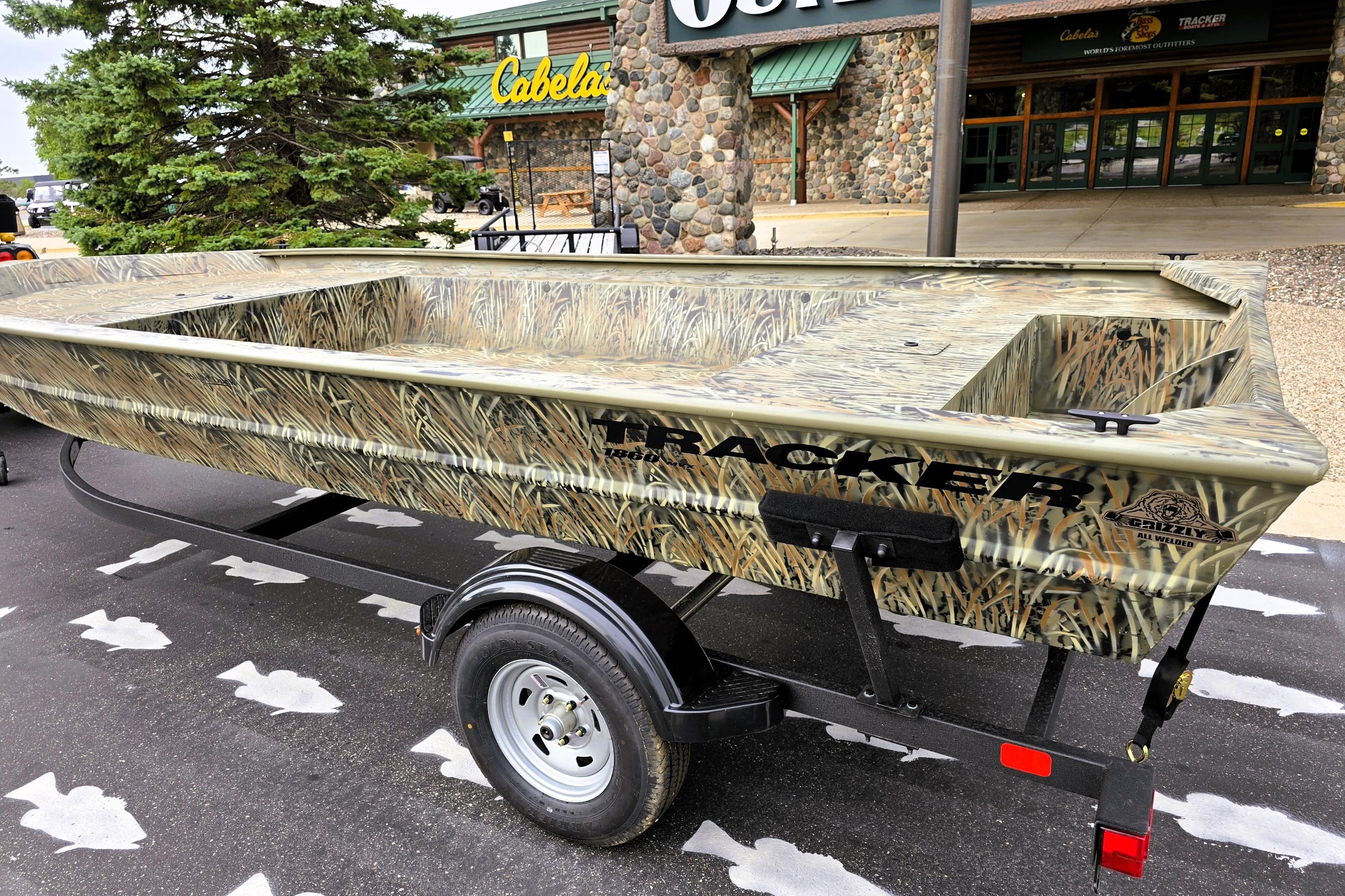 2026 Tracker GRIZZLY 1860 Utility boat with camouflage design on a trailer outside Cabela's store.