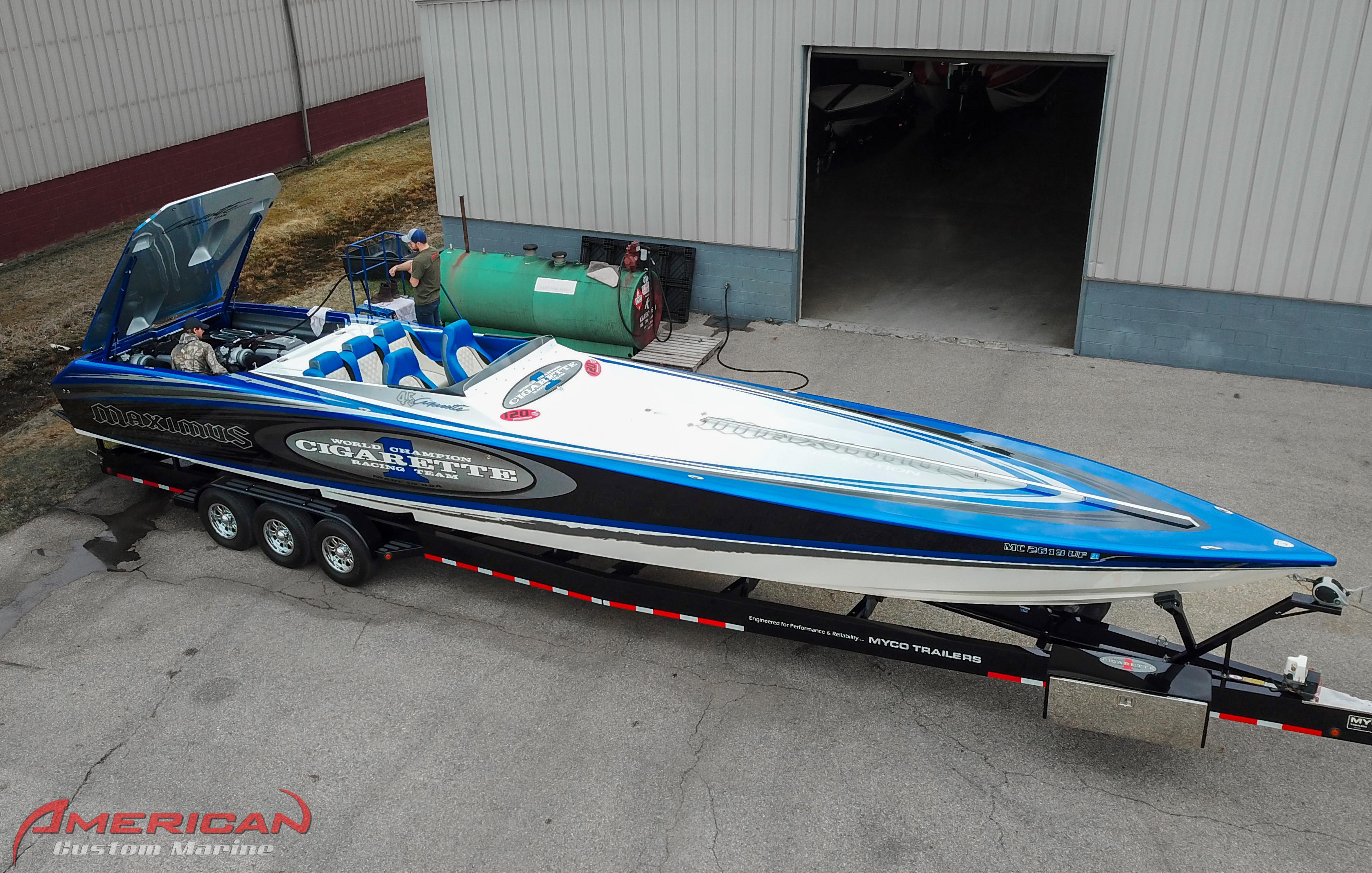 2005 Cigarette 45 Maximus speedboat on trailer, blue and white design, parked outside a building.
