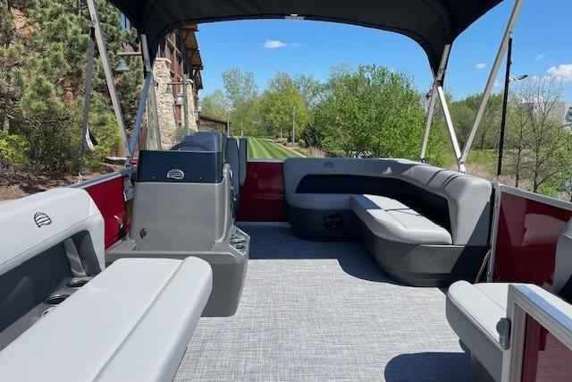 2026 Sun Tracker Party Barge 16 DLX interior with seating and canopy, surrounded by greenery.