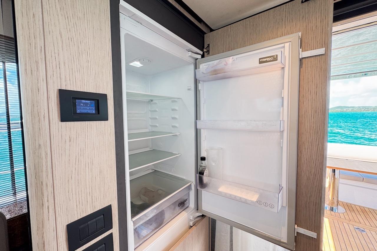 Open refrigerator on 2024 Ferretti Yachts 580, showcasing modern interior and ocean view.