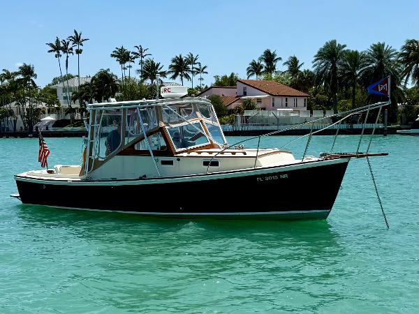 1978 Dyer 29 Trunk Cabin boat on turquoise water, with palm trees in the background.
