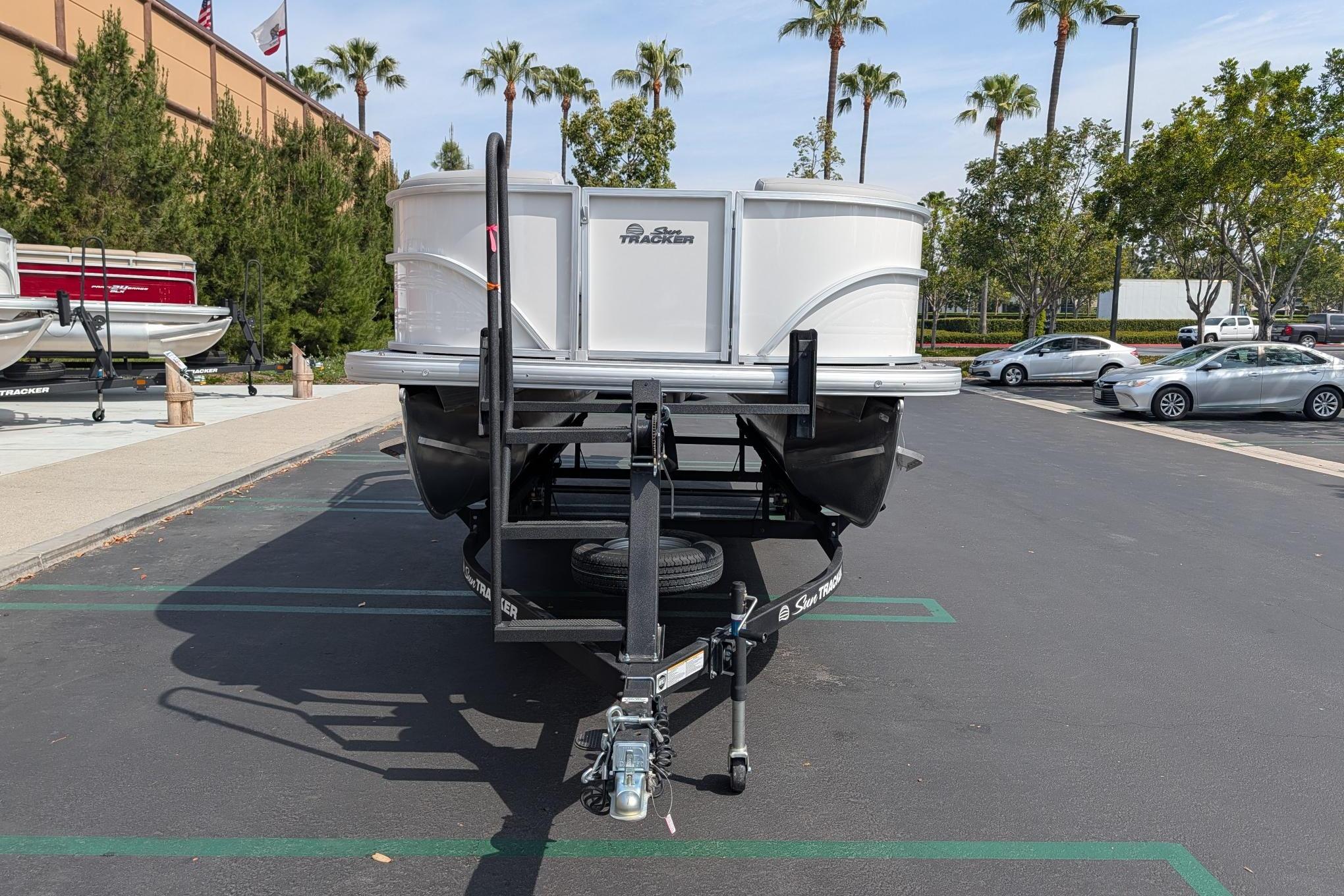 2026 Sun Tracker Party Barge 20 DLX pontoon boat on trailer in parking lot.