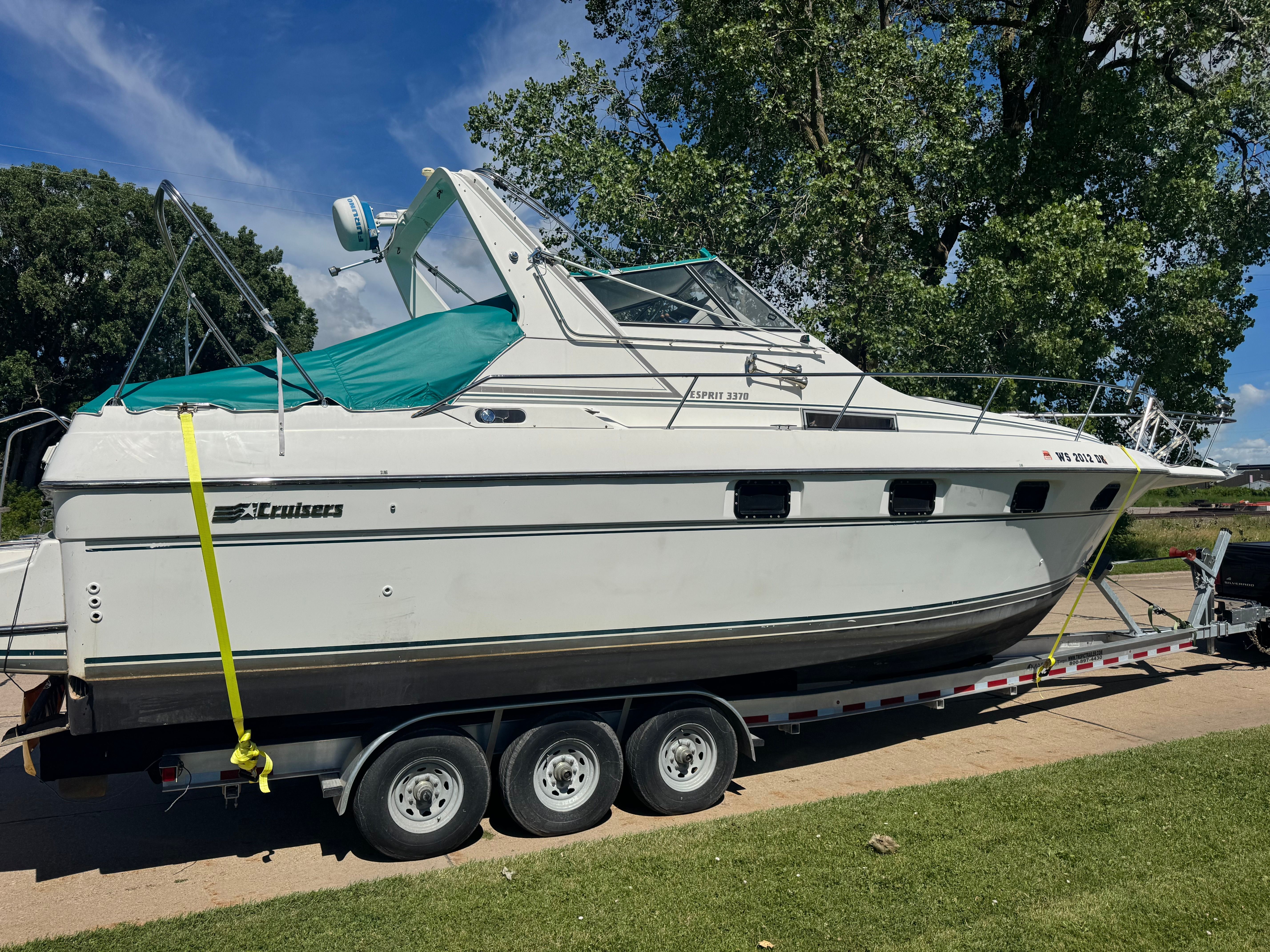 A 1992 Cruisers Yachts Esprit 3370 on a trailer, surrounded by trees and grass.