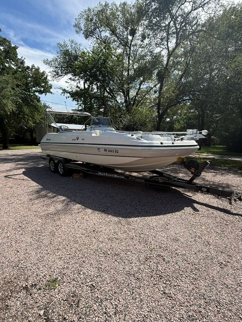 A 2016 Hurricane SunDeck Sport 231 OB boat on a trailer on a gravel path.