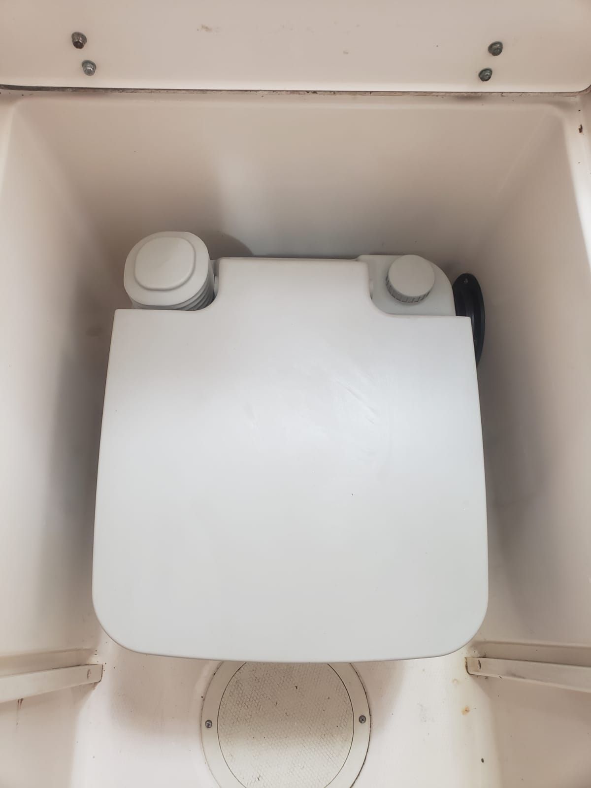 A portable toilet system in a boat compartment, surrounded by white walls.