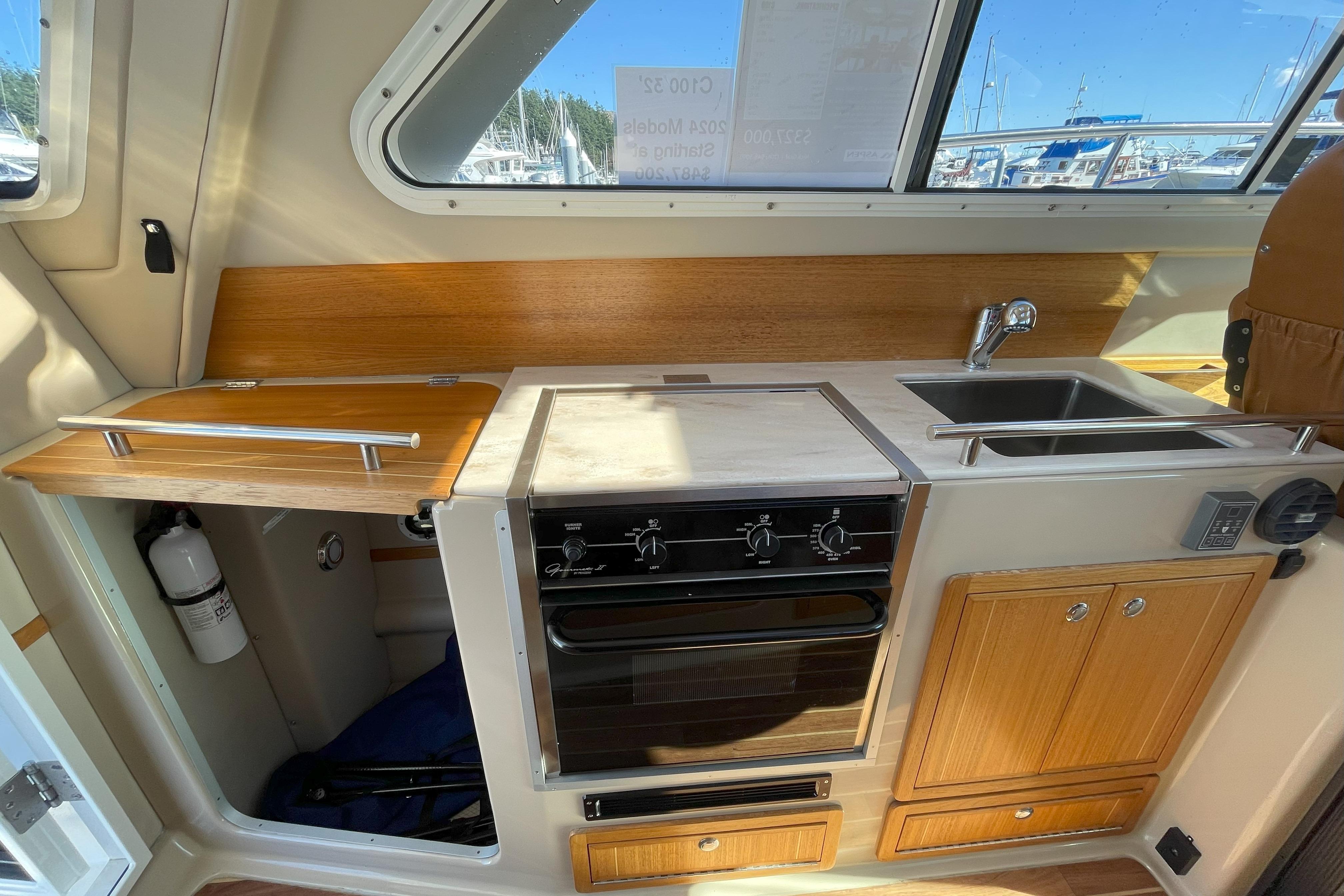 Compact kitchen in 2015 Aspen C100 boat with stove, sink, and wooden cabinetry.