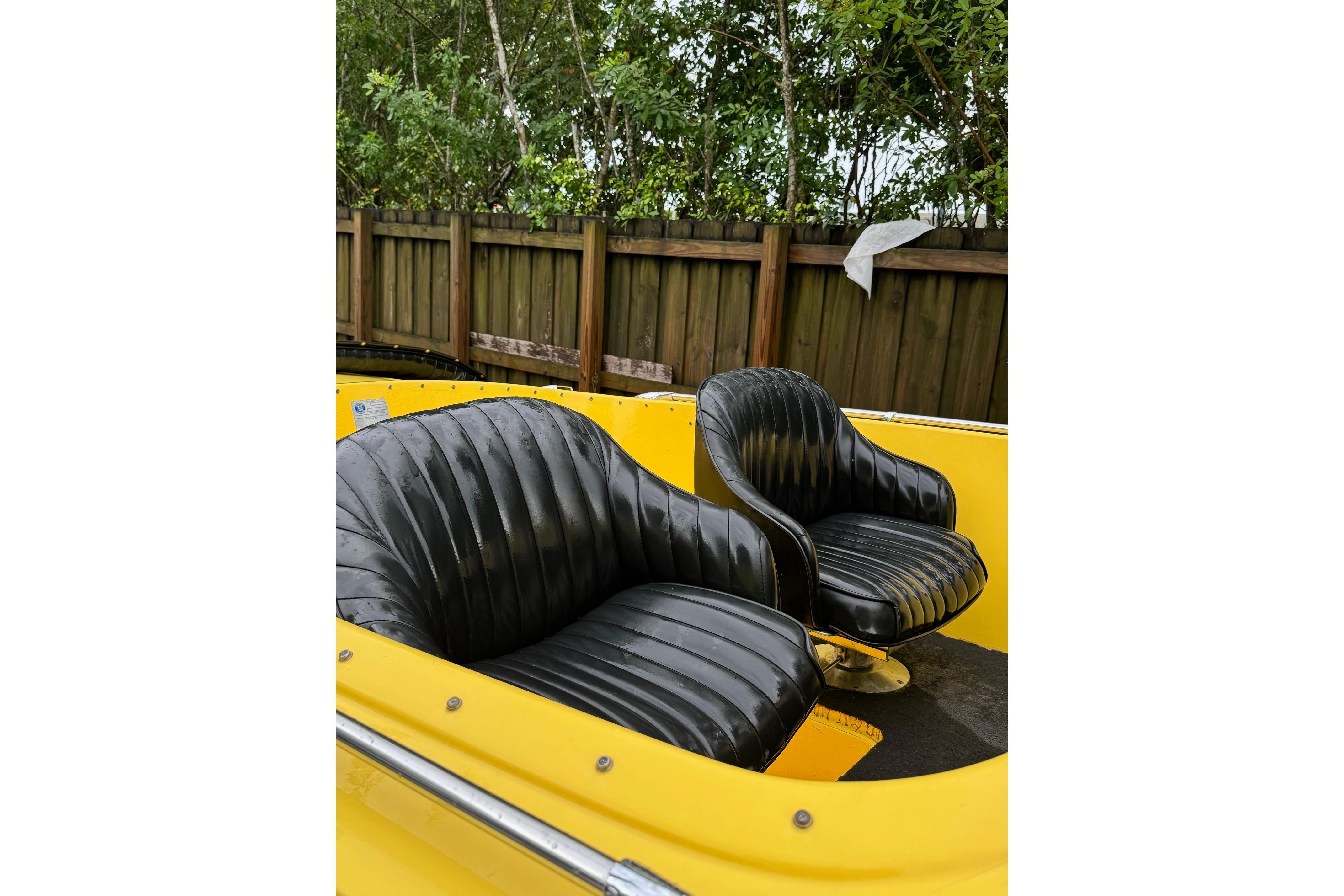 Yellow 1987 Donzi 16 Classic boat with black leather seats, wooden fence background.