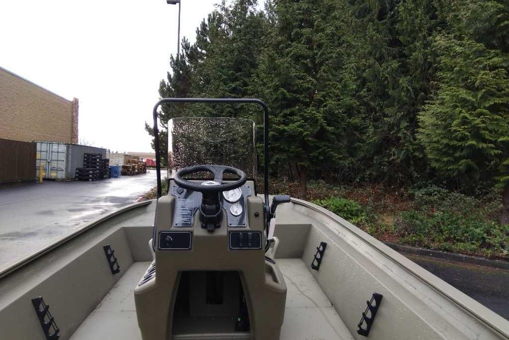 2026 Tracker Grizzly 1860 CC boat, steering console view, parked near trees and industrial area.