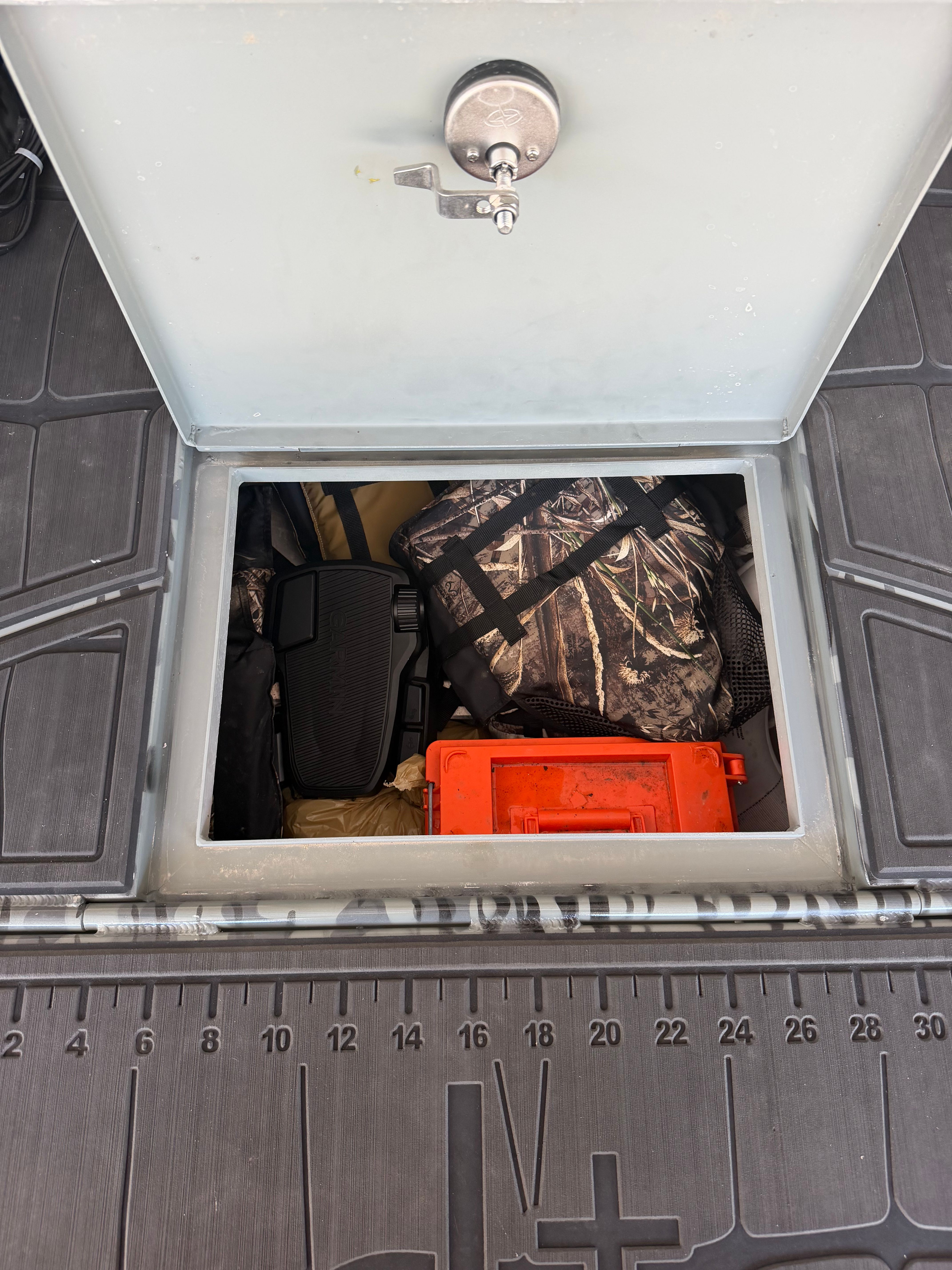 An open storage compartment on a boat with gear and an orange box.