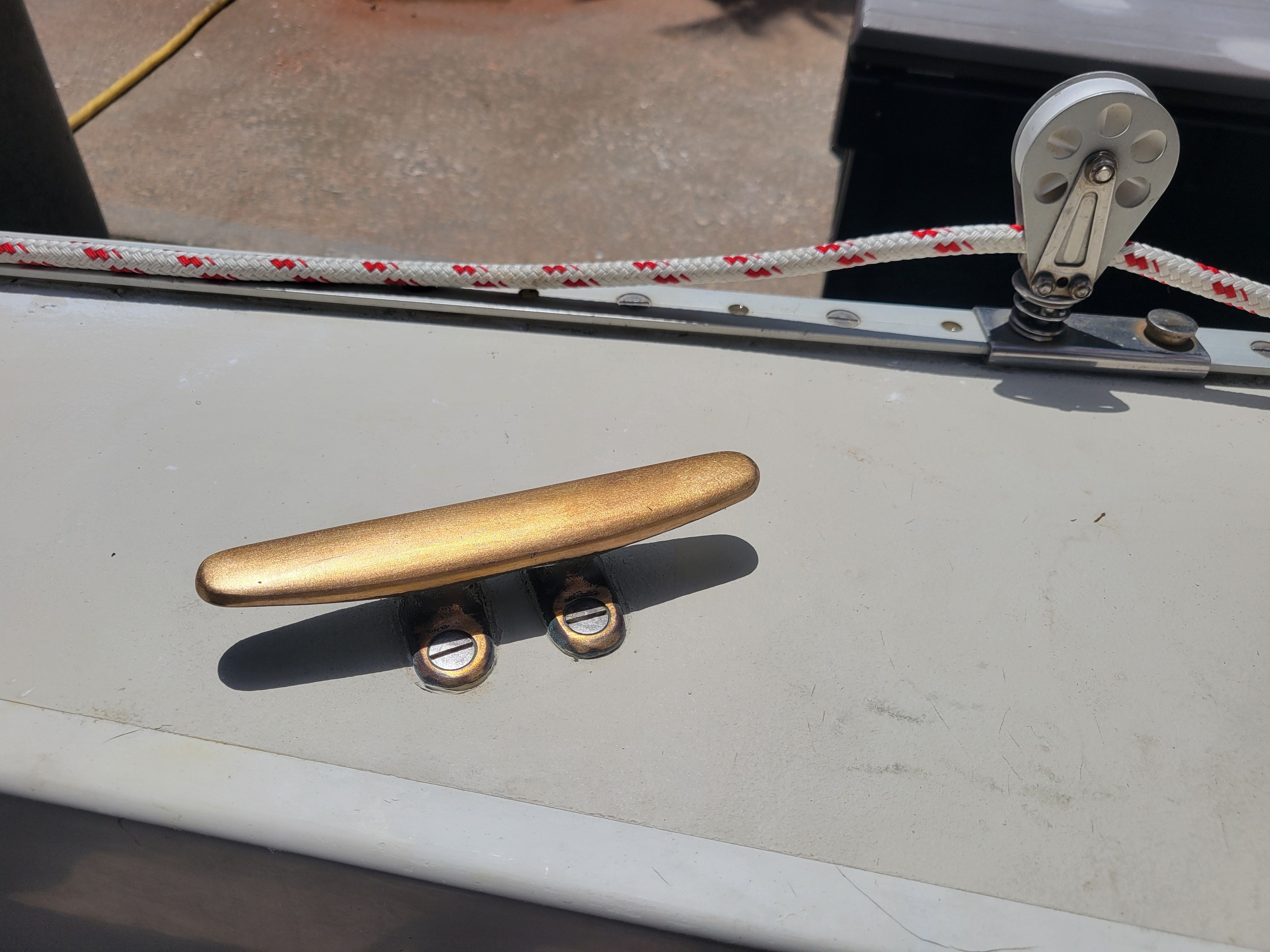 Close-up of a golden cleat on a boat, with a rope and pulley nearby.