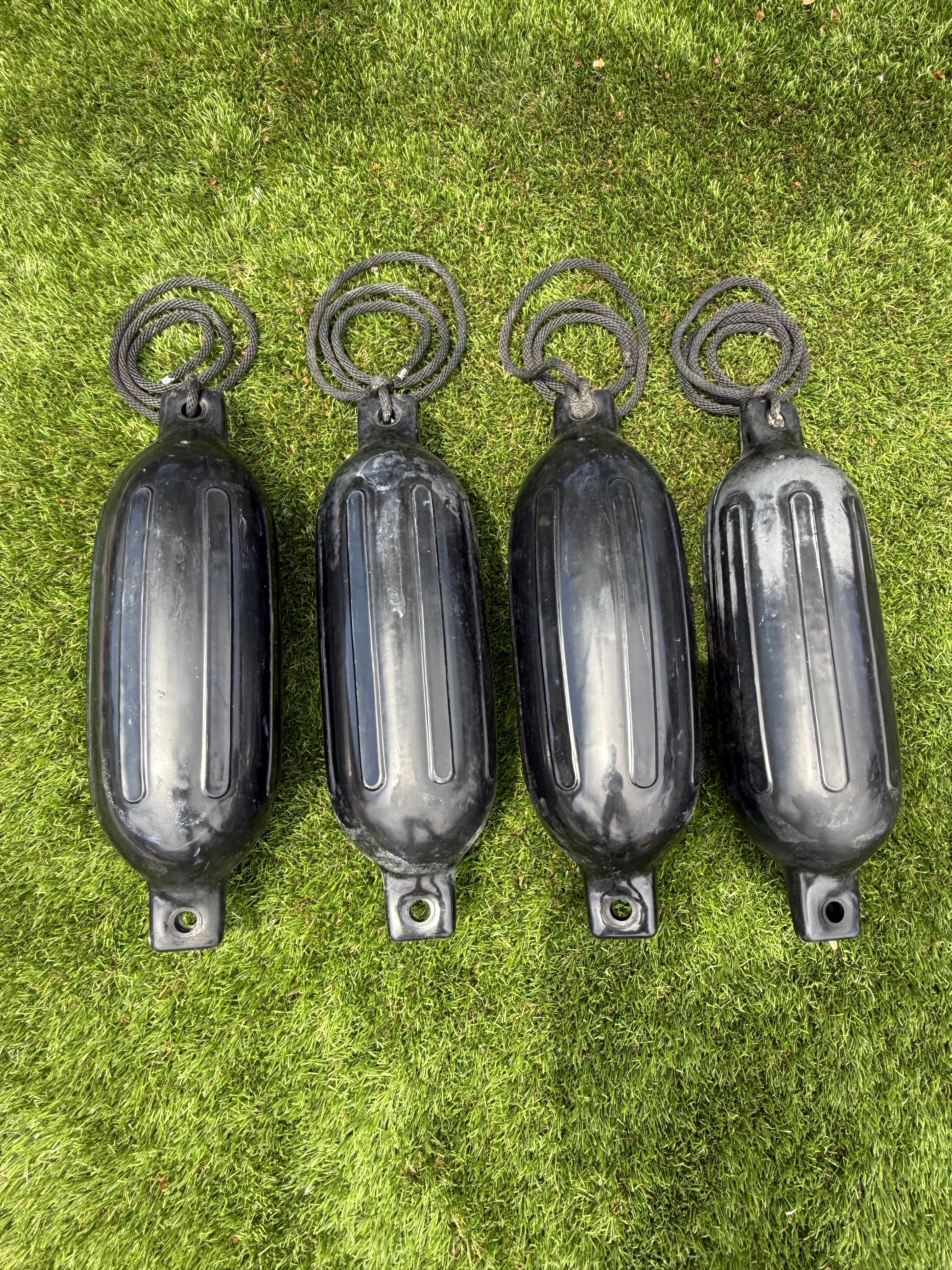 Four black boat fenders on green grass.