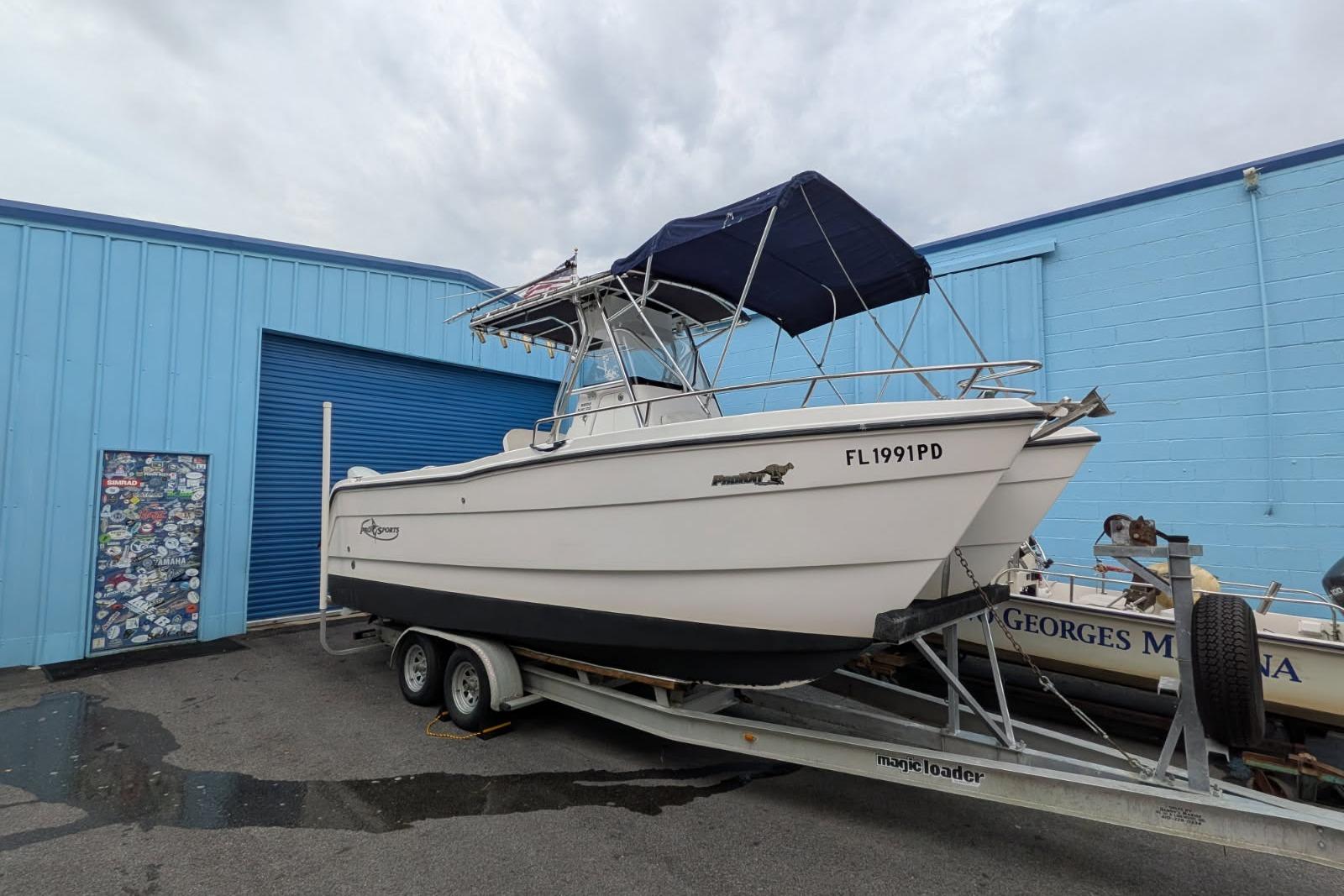 2002 Pro Sports 2200 CC ProKat boat on trailer, parked near blue building.