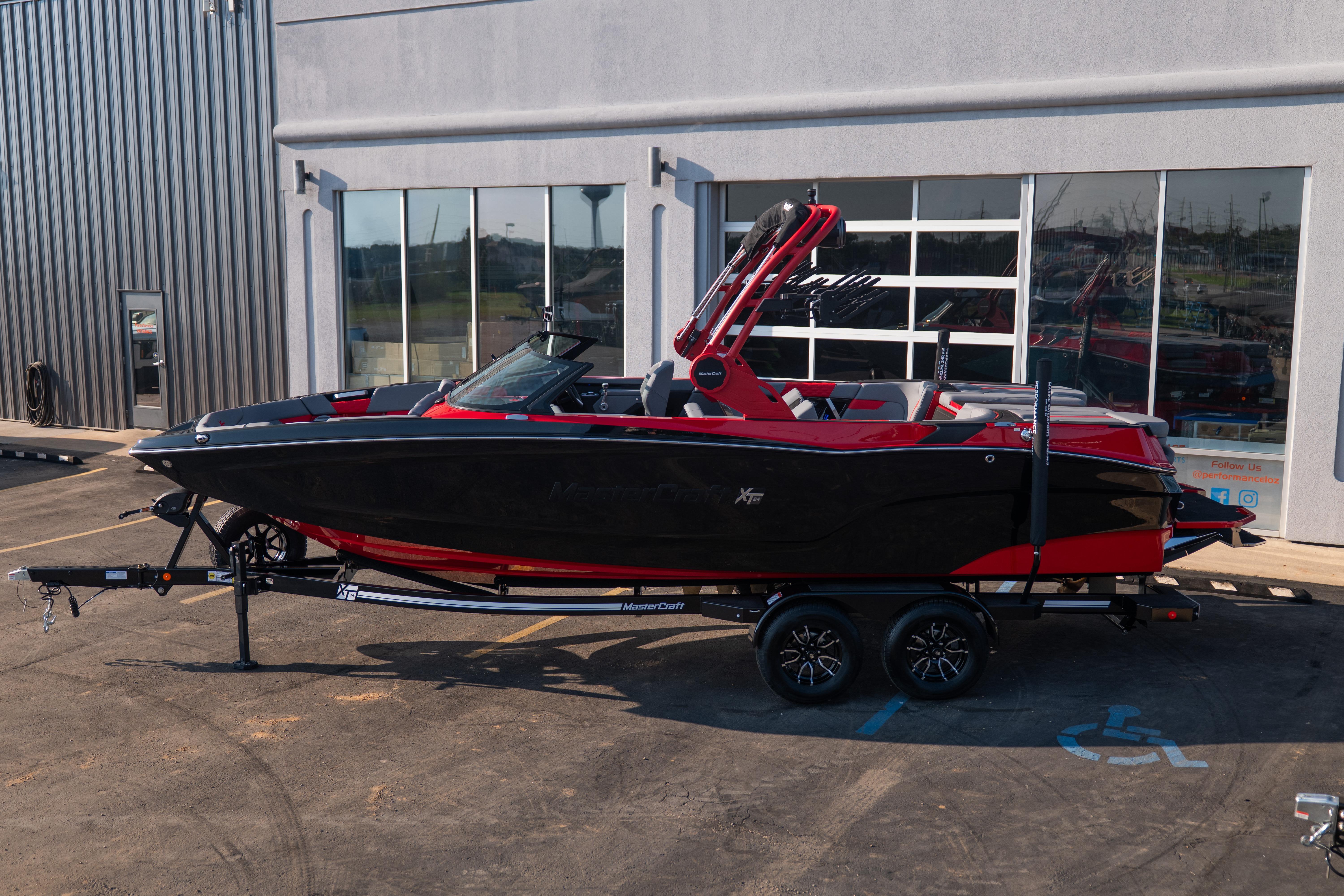 2027 MasterCraft XT24 boat in black and red on a trailer outside a building.