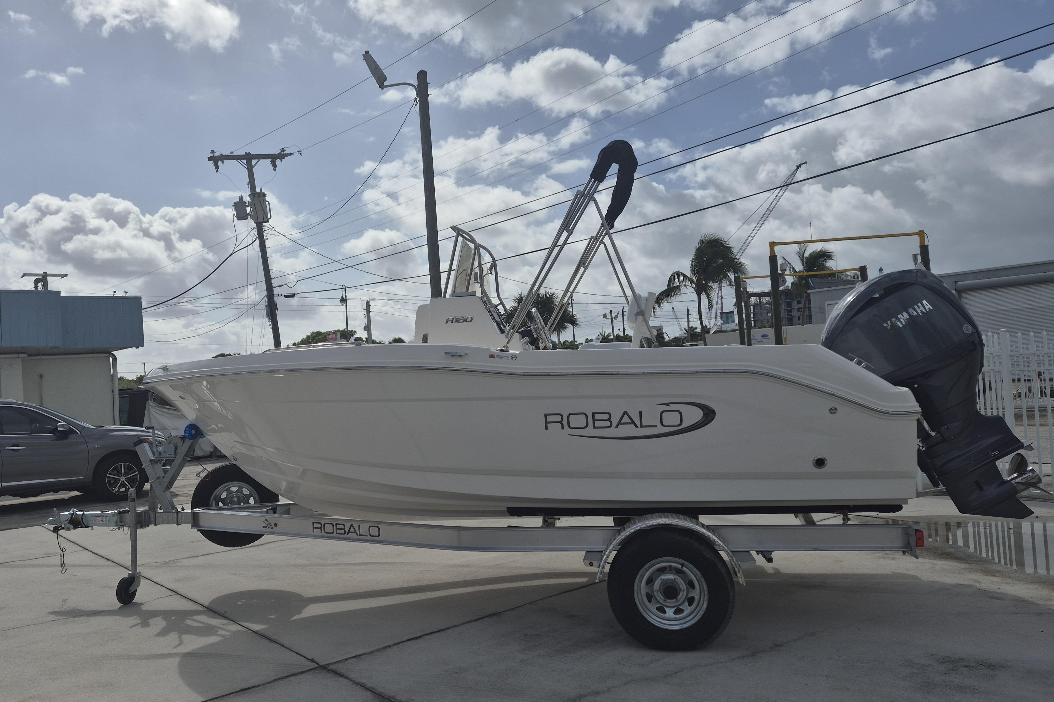 2026 Robalo R180 Center Console boat on trailer, parked outdoors under cloudy sky.