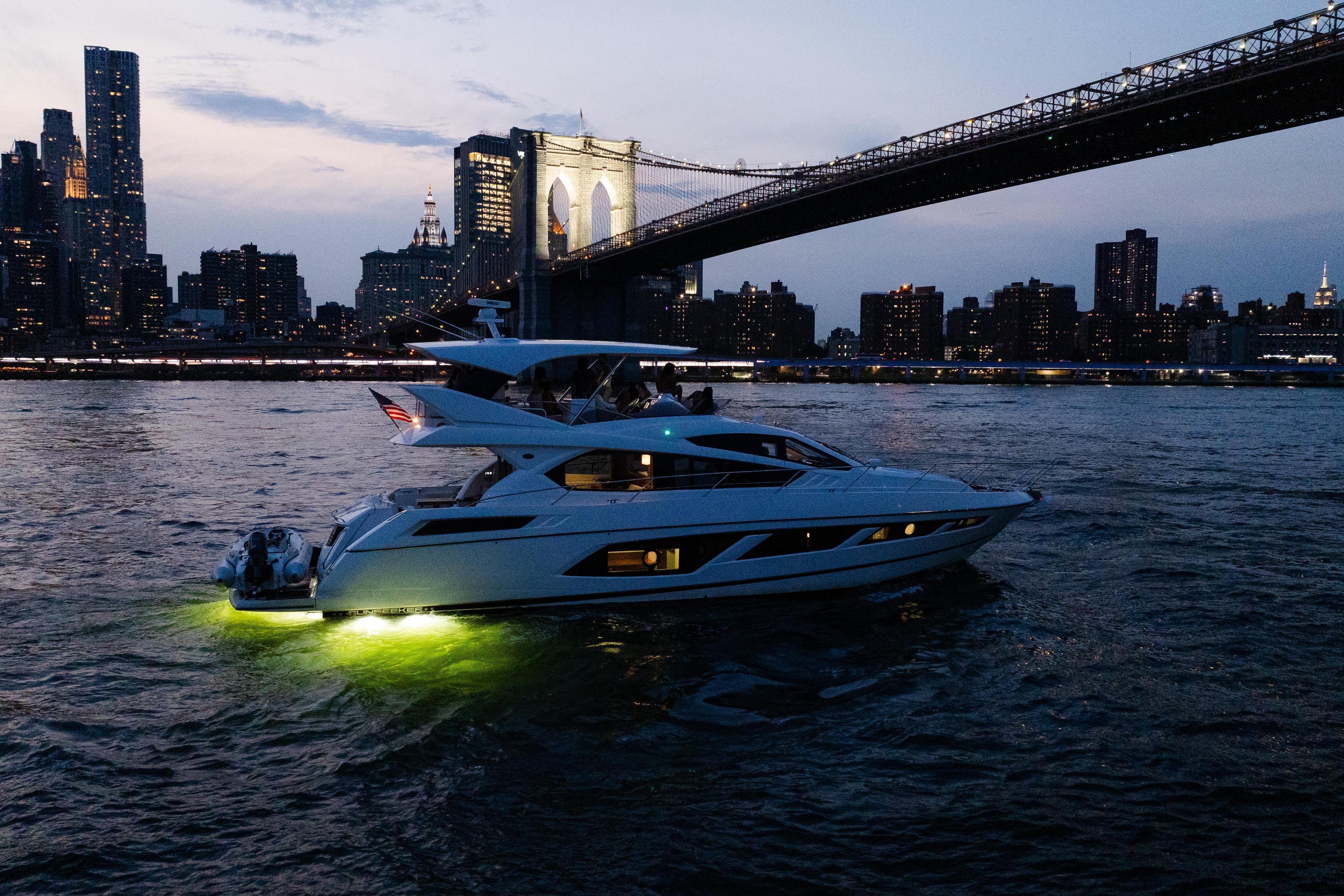 Luxurious 2016 Sunseeker Manhattan 65 yacht cruising under Brooklyn Bridge at dusk.