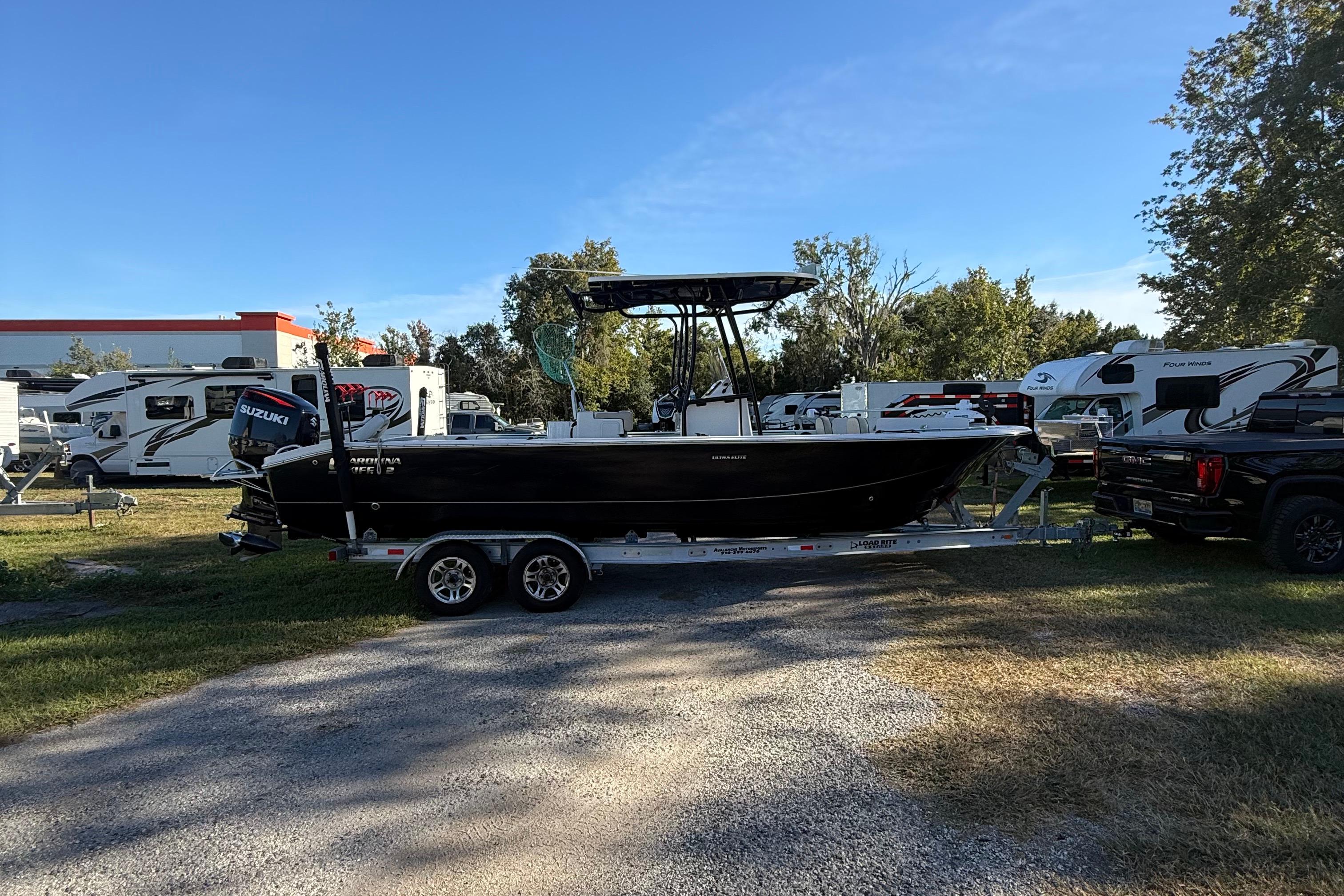 2021 Carolina Skiff 26 Ultra Elite boat on trailer, parked outdoors near RVs.