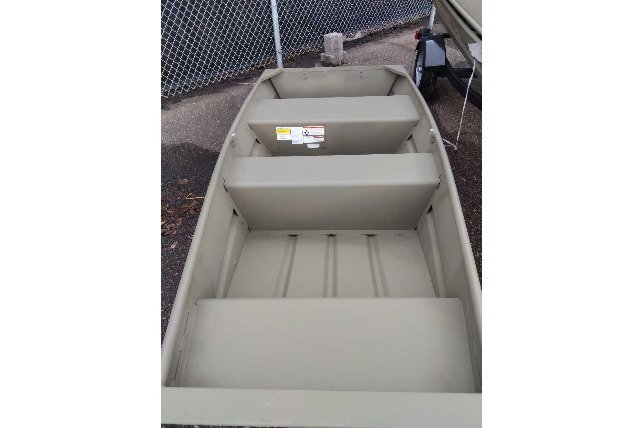 2026 Tracker Grizzly 10 Jon boat, olive green, parked on pavement near chain-link fence.