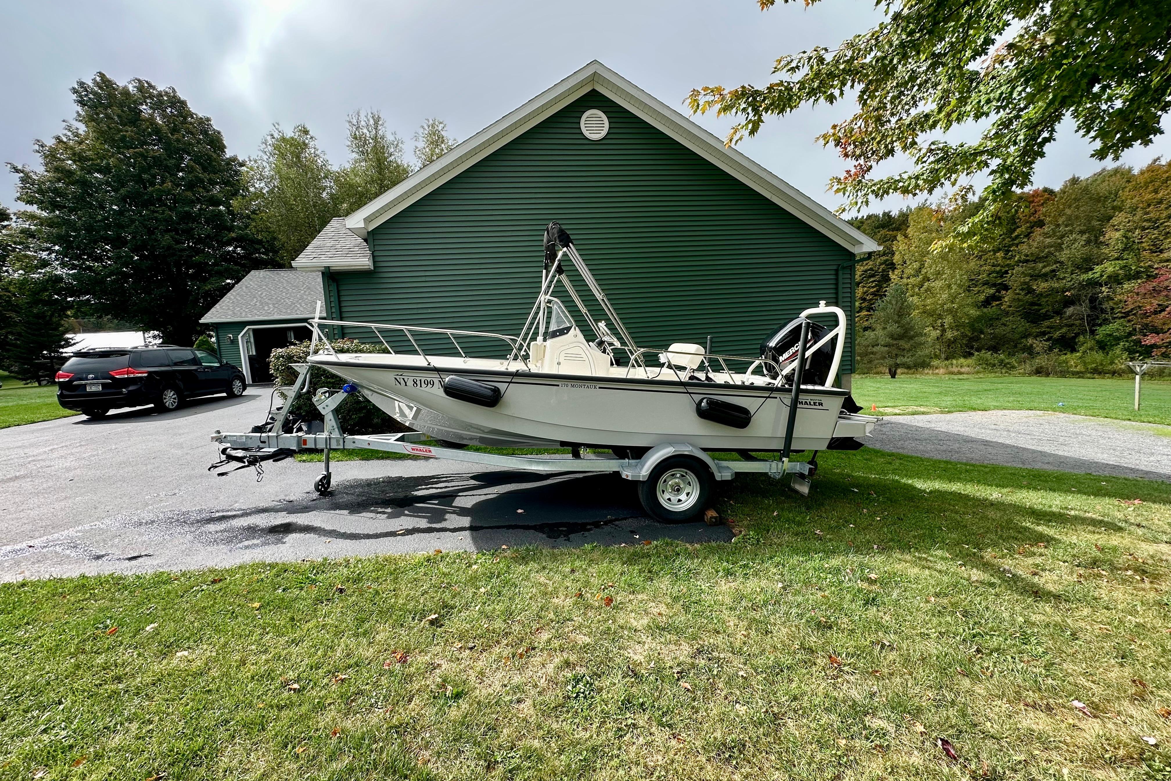 2024 Boston Whaler 170 Montauk boat on trailer, parked near green house.