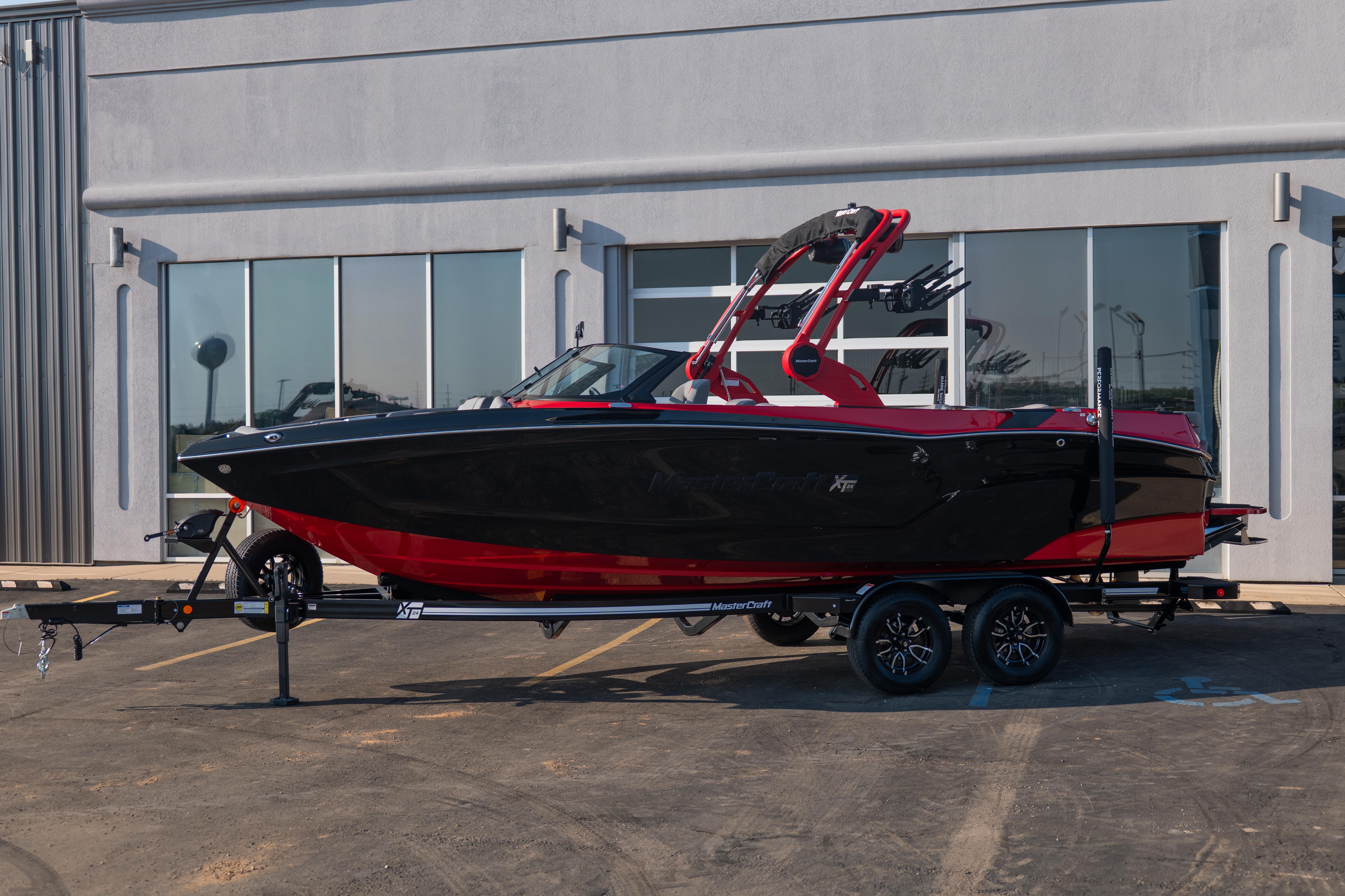 2027 MasterCraft XT24 boat in black and red on a trailer, parked outside a building.