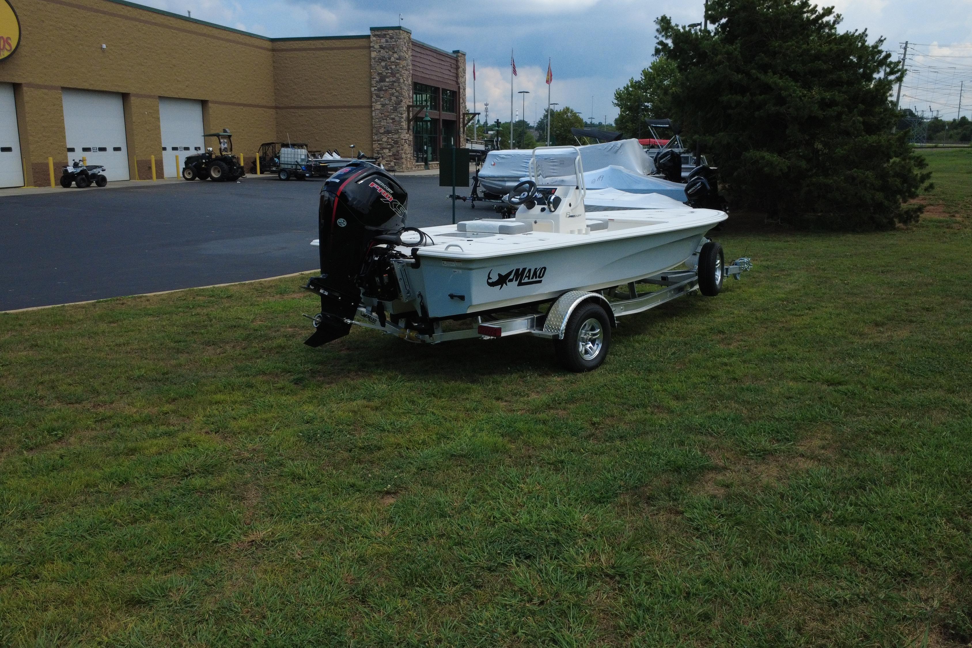 2026 Mako 18 Pro Skiff boat on trailer, parked on grass near a building.