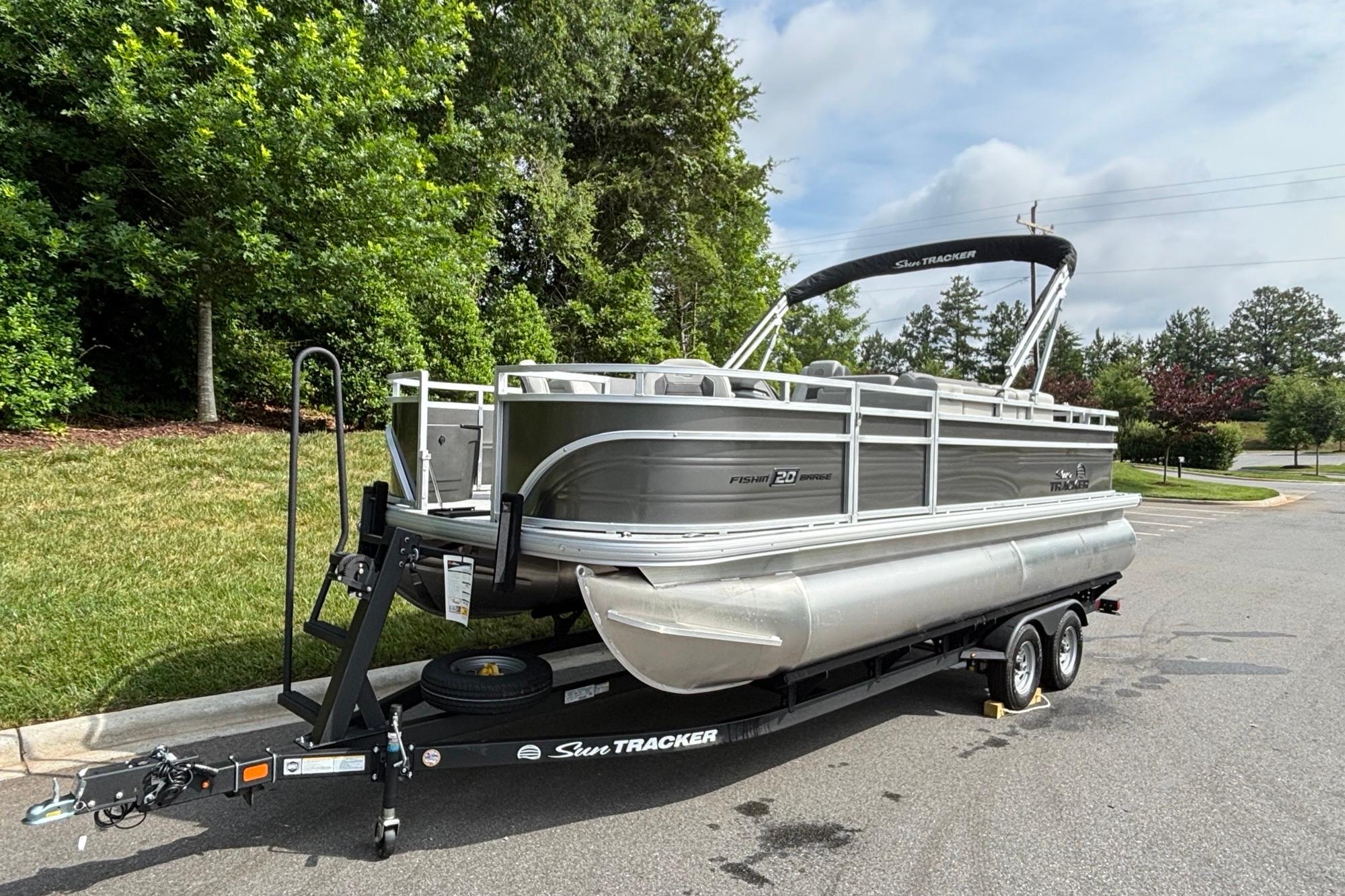 2026 Sun Tracker Fishin' Barge 20 DLX pontoon boat on trailer, parked outdoors.