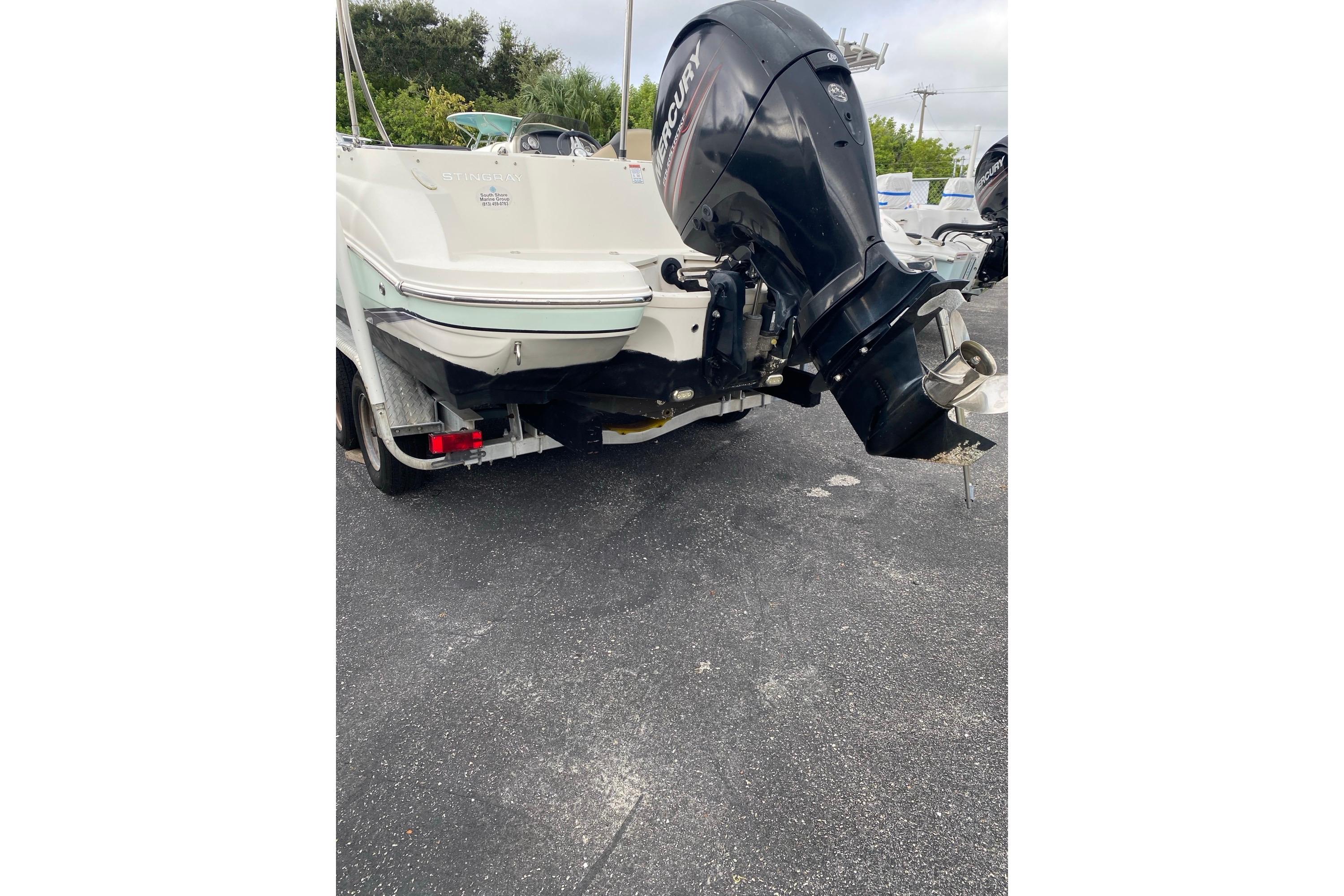 2018 Stingray 212 SC boat with Mercury outboard motor, parked on asphalt.