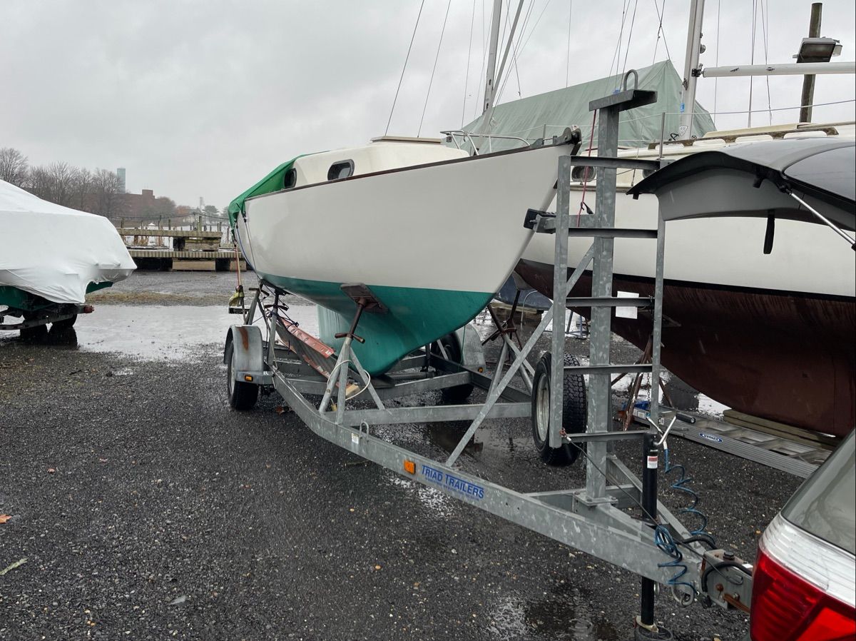 A 1981 Cape Dory 22-1 sailboat is on a trailer in a gravel lot.