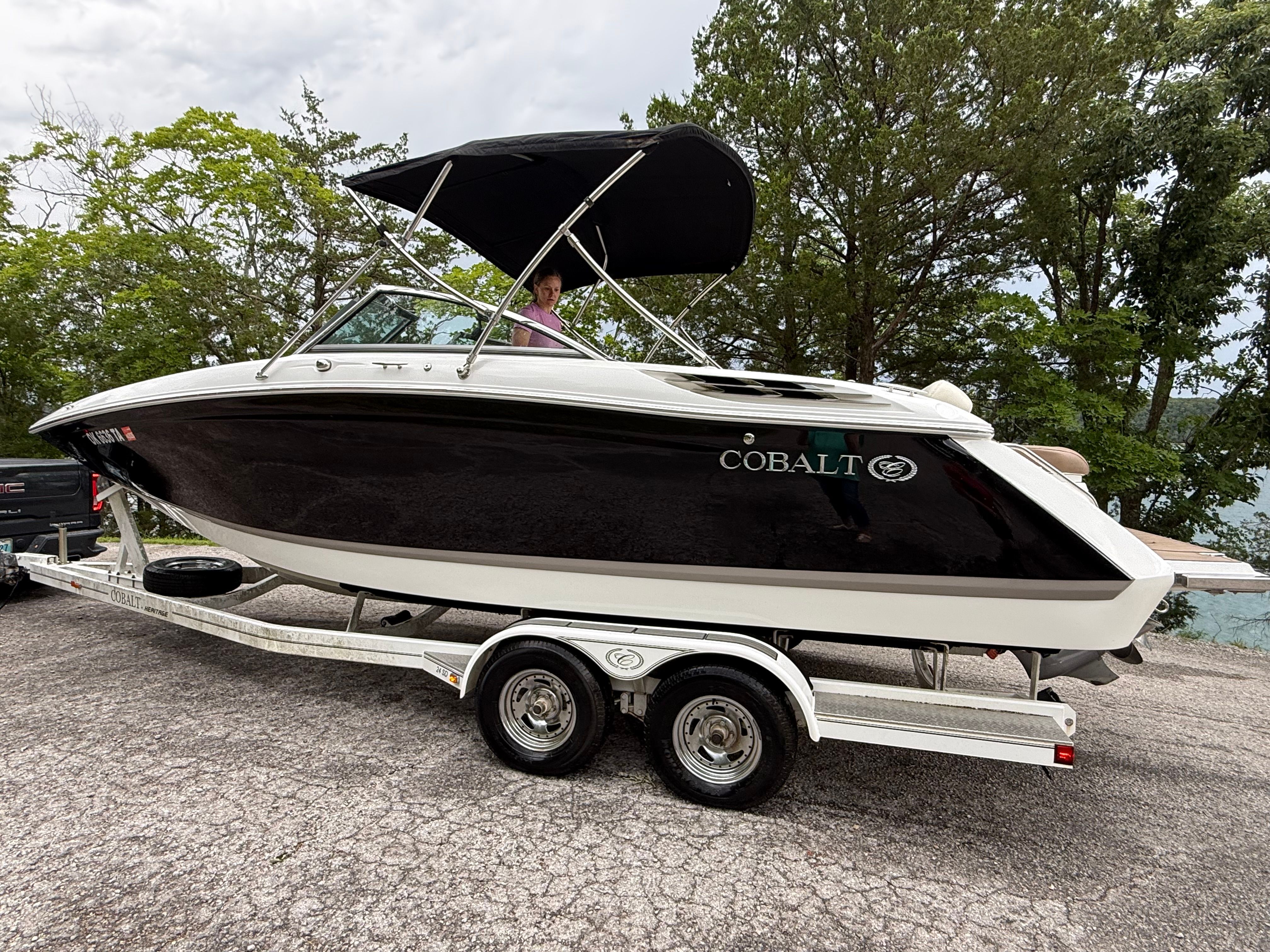 A 2015 Cobalt boat on a trailer, surrounded by trees.