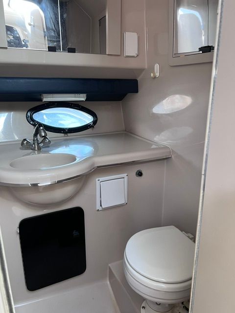 Interior view of a boat bathroom with sink, toilet, and porthole.