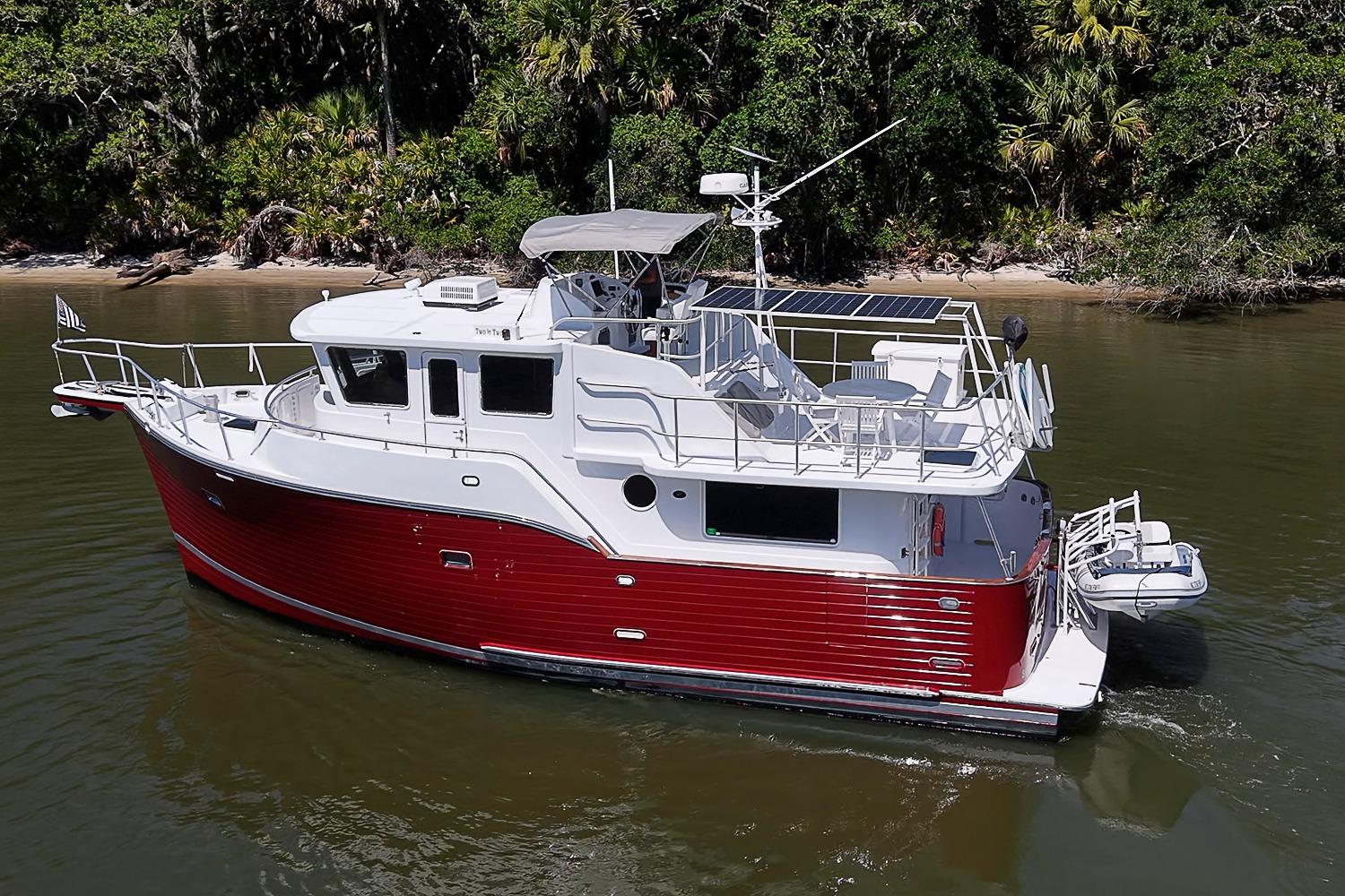 2003 Magna Marine Nova Scotia 47 boat with red hull cruising near lush shoreline.
