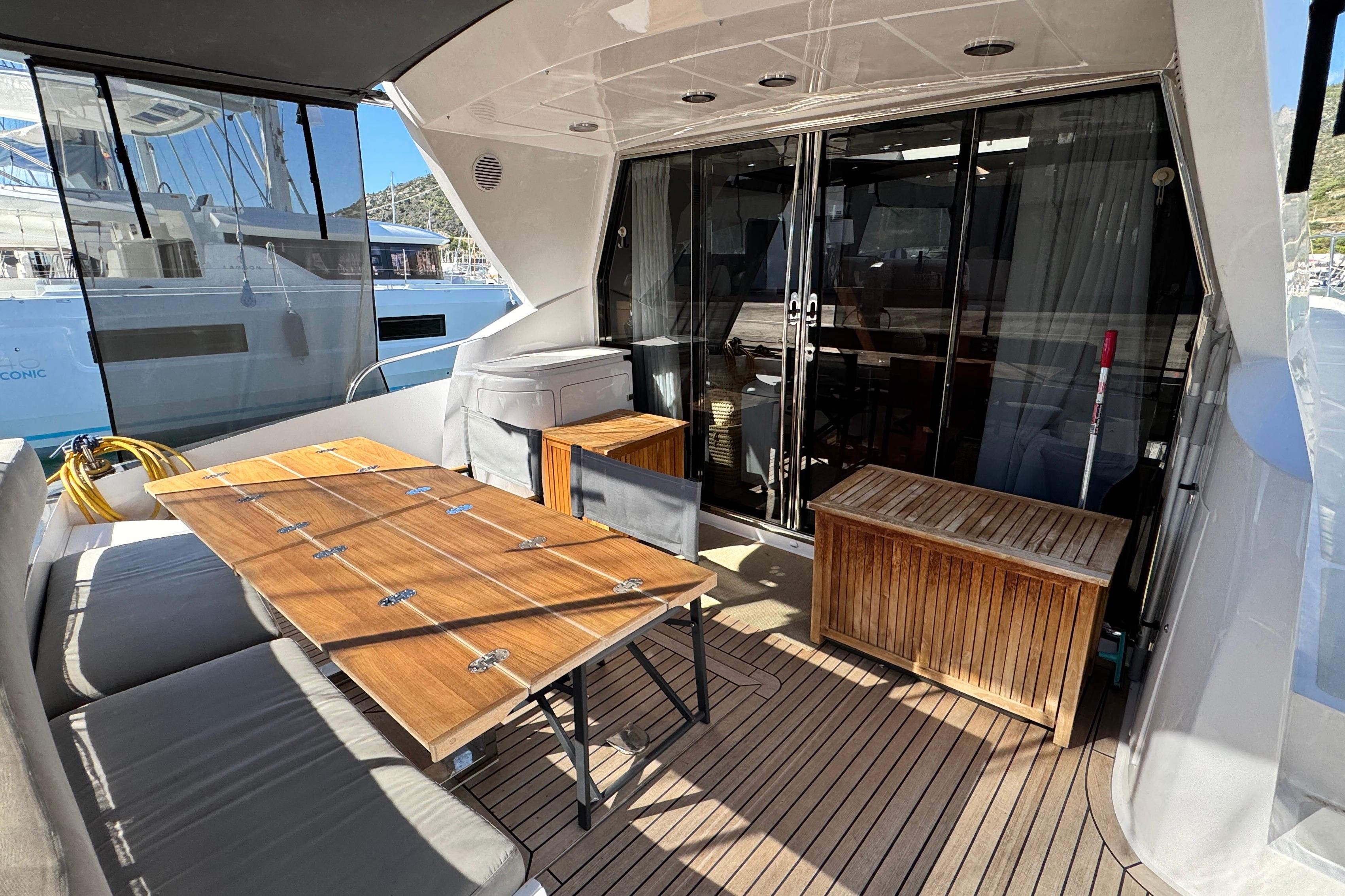 Luxurious 2007 Doma 5 yacht deck with wooden furniture and glass doors.