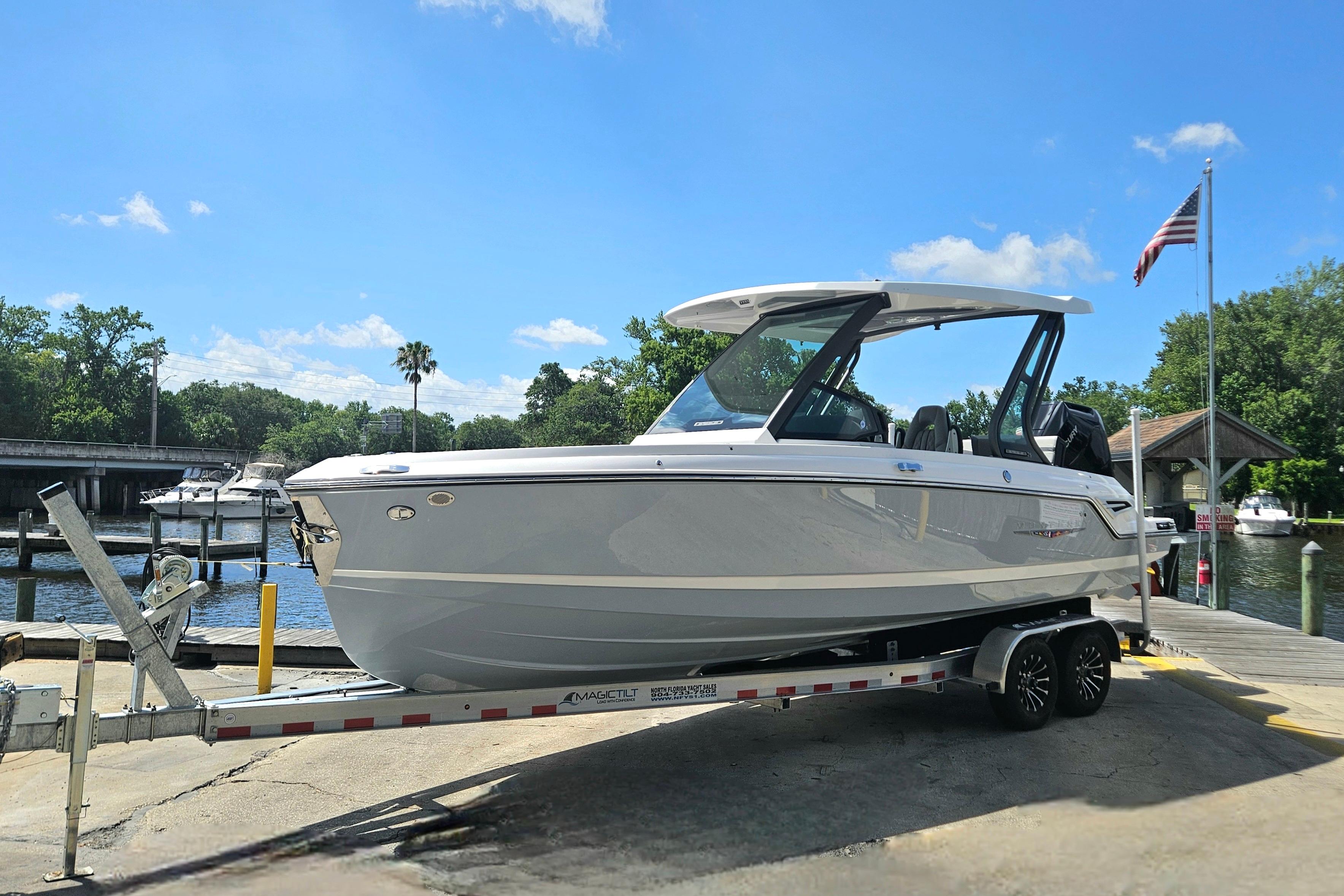 2026 Monterey Elite 25 OB boat on trailer by waterfront, under clear blue sky.
