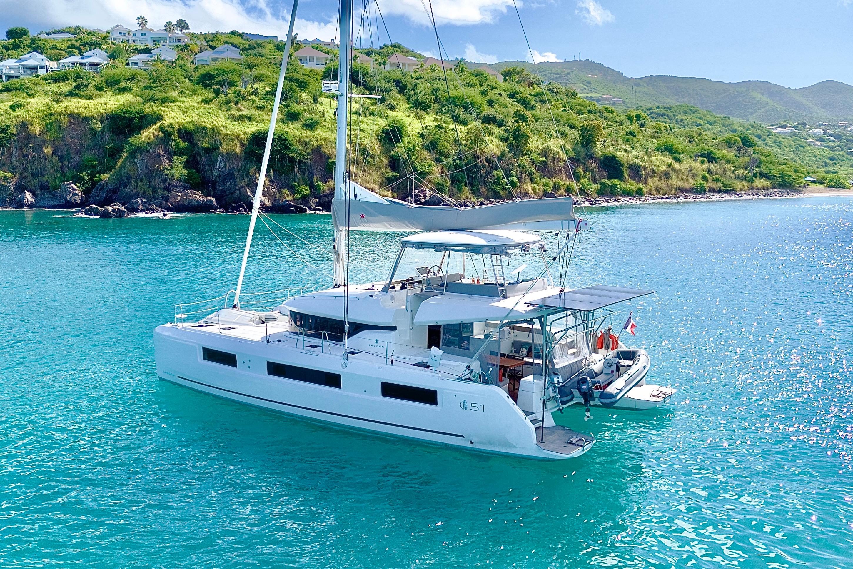 2024 Lagoon 51 catamaran anchored in turquoise waters near lush green coastline.