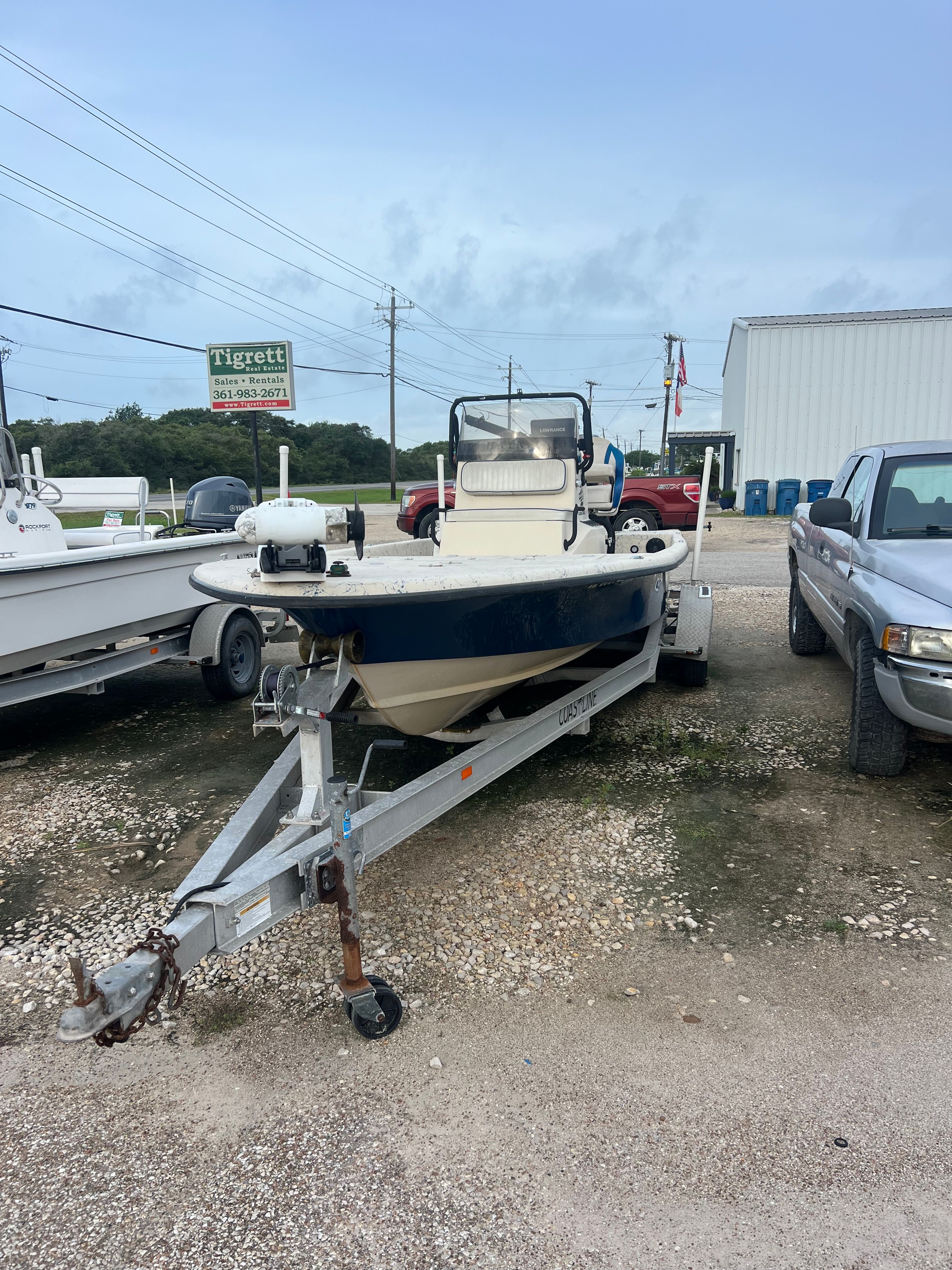 2014 Haynie ho boat on a trailer, parked on a gravel lot next to a pickup truck.