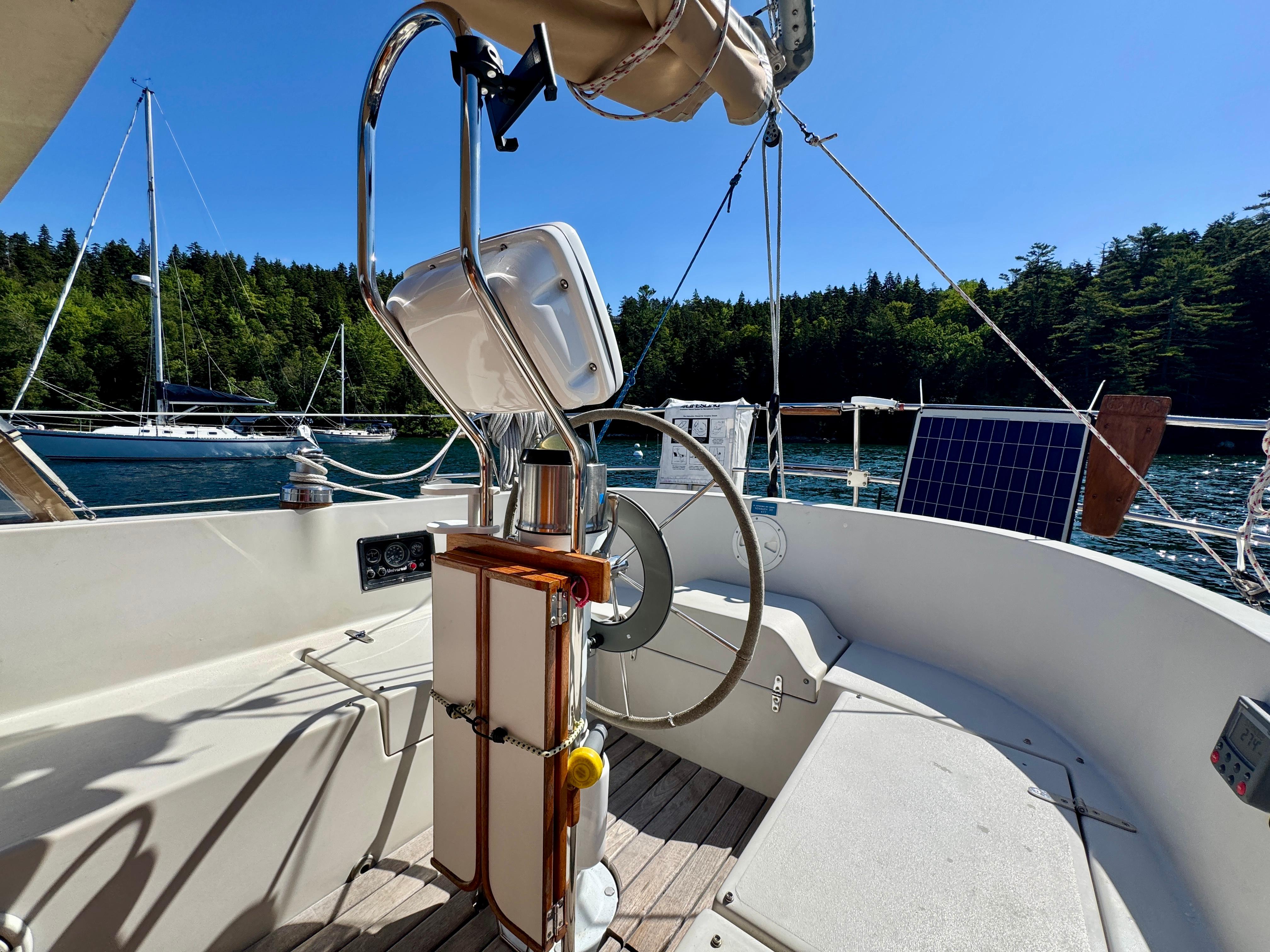 1989 Nonsuch 30 Ultra sailboat cockpit with steering wheel, solar panel, and scenic water view.