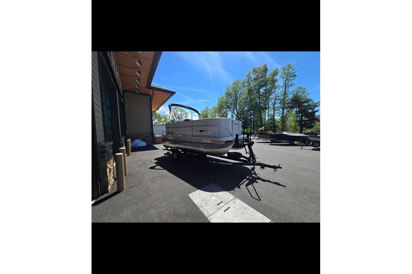 2026 Sun Tracker Party Barge 16 DLX on trailer, parked outdoors under clear blue sky.