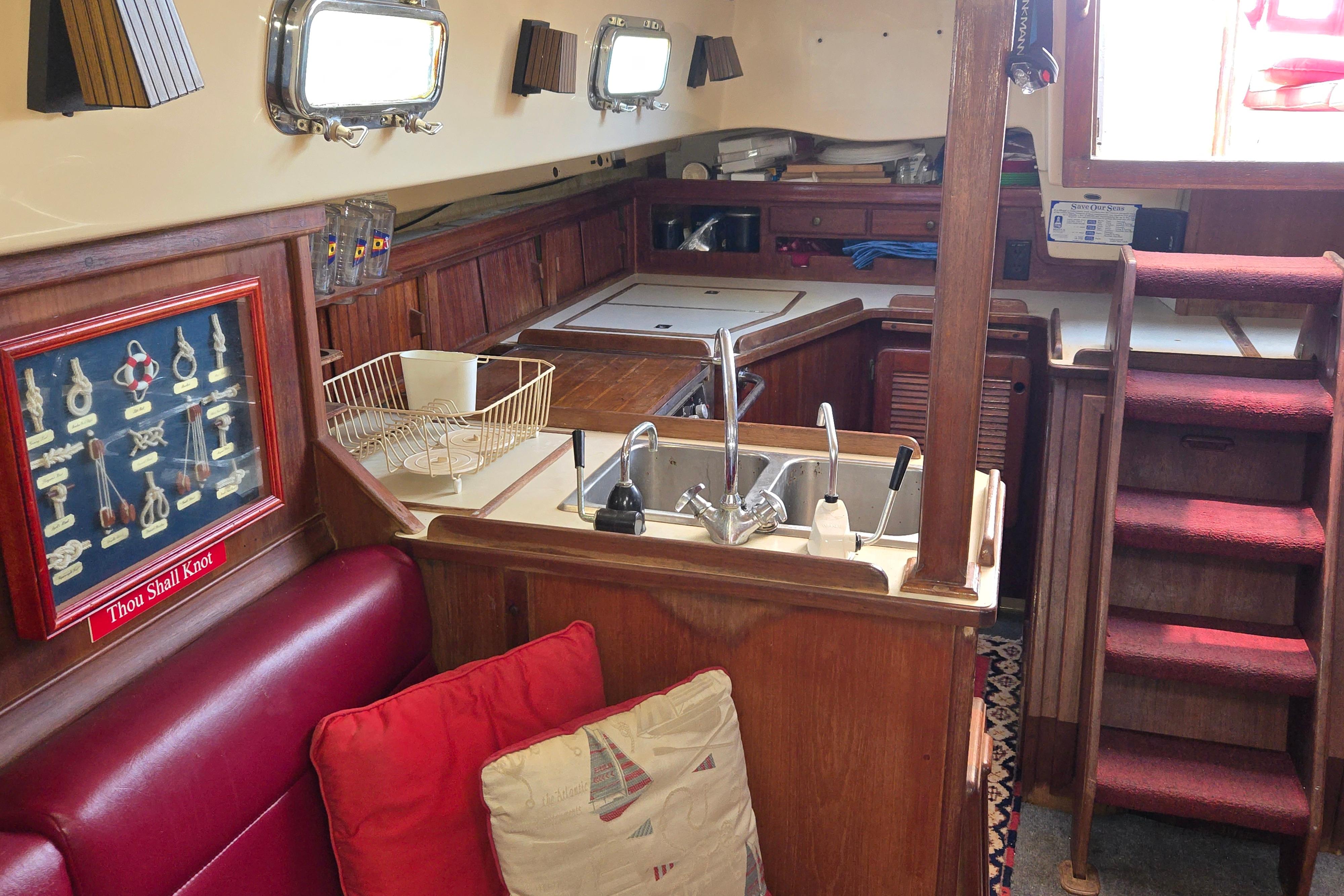 Interior of 1989 Island Packet 35 sailboat with wooden cabinetry and compact kitchen area.