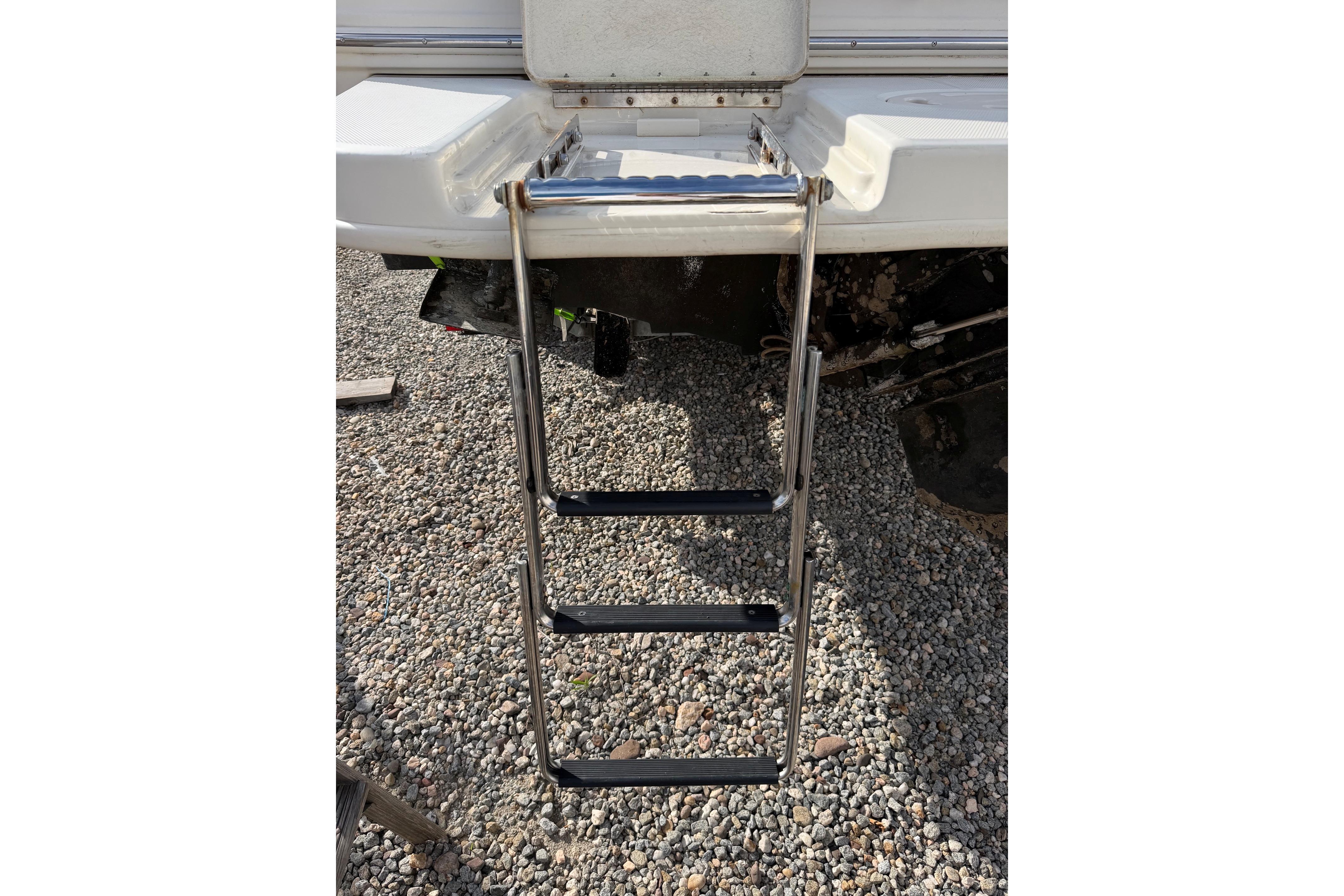 Stainless steel swim ladder on 2000 Sea Ray 240 Sundancer boat, resting on gravel.
