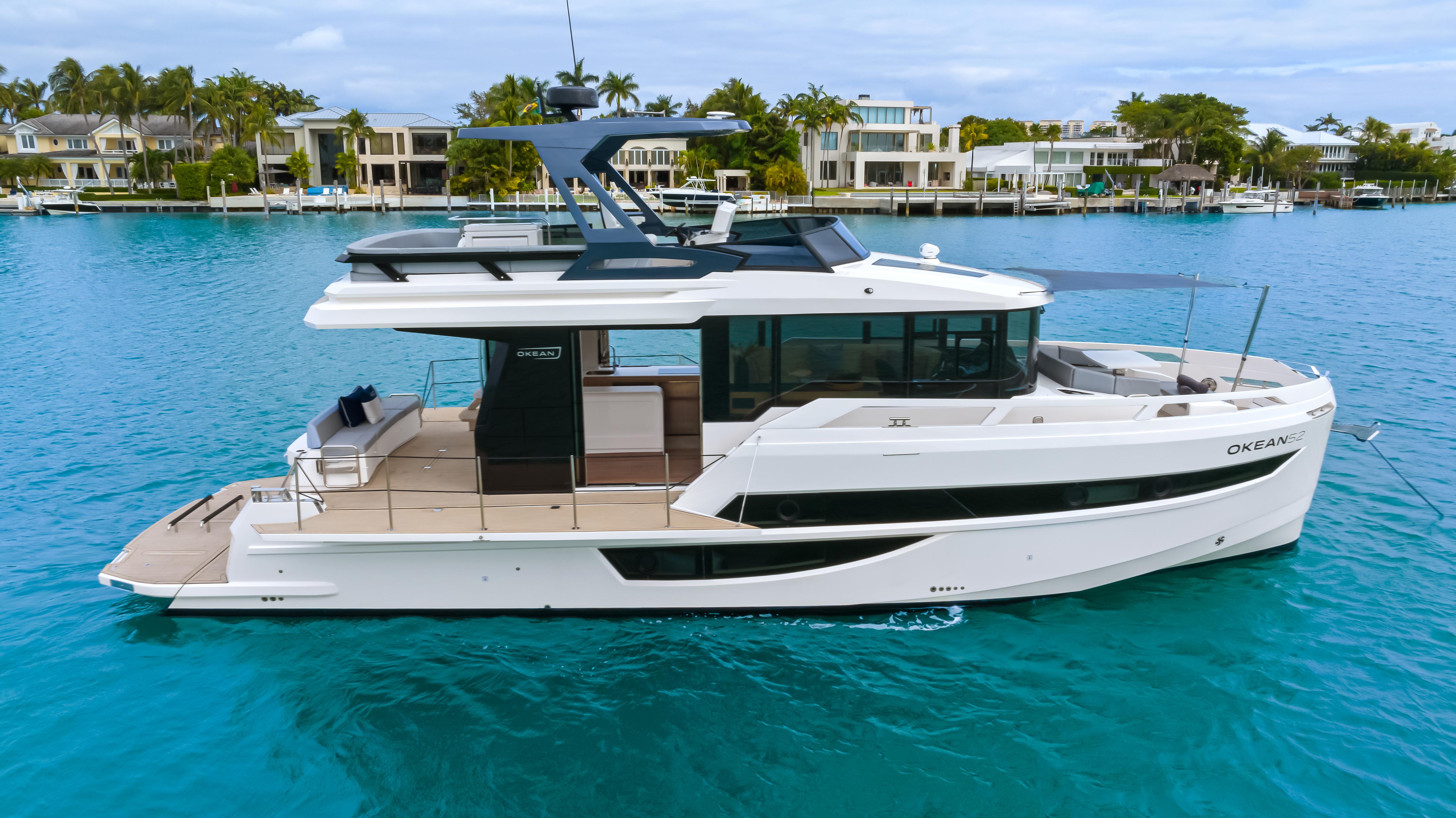 2025 OKEAN 52 yacht on turquoise water near luxury waterfront homes.