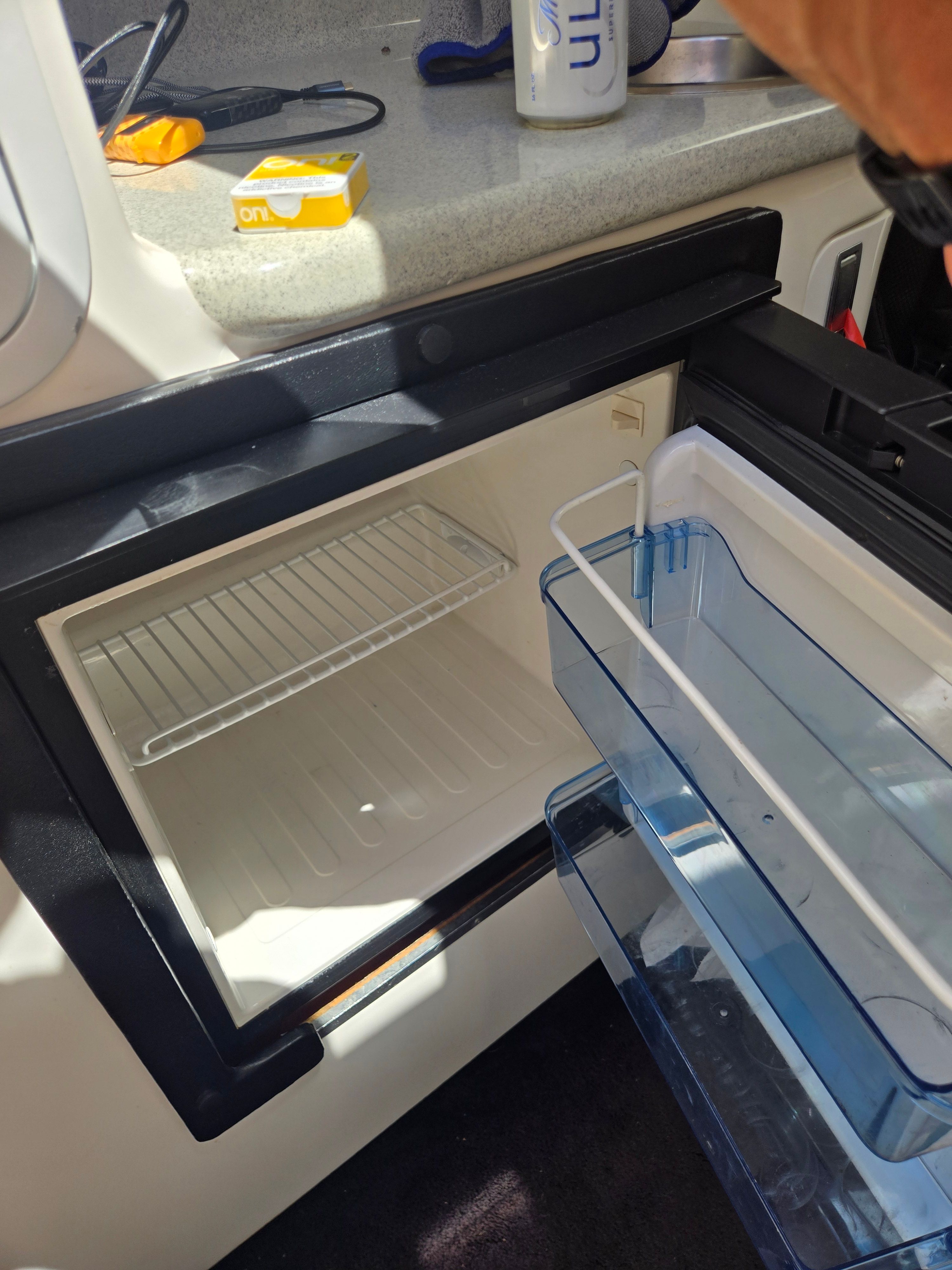 An open fridge in a boat with an empty shelf and a blue drawer.