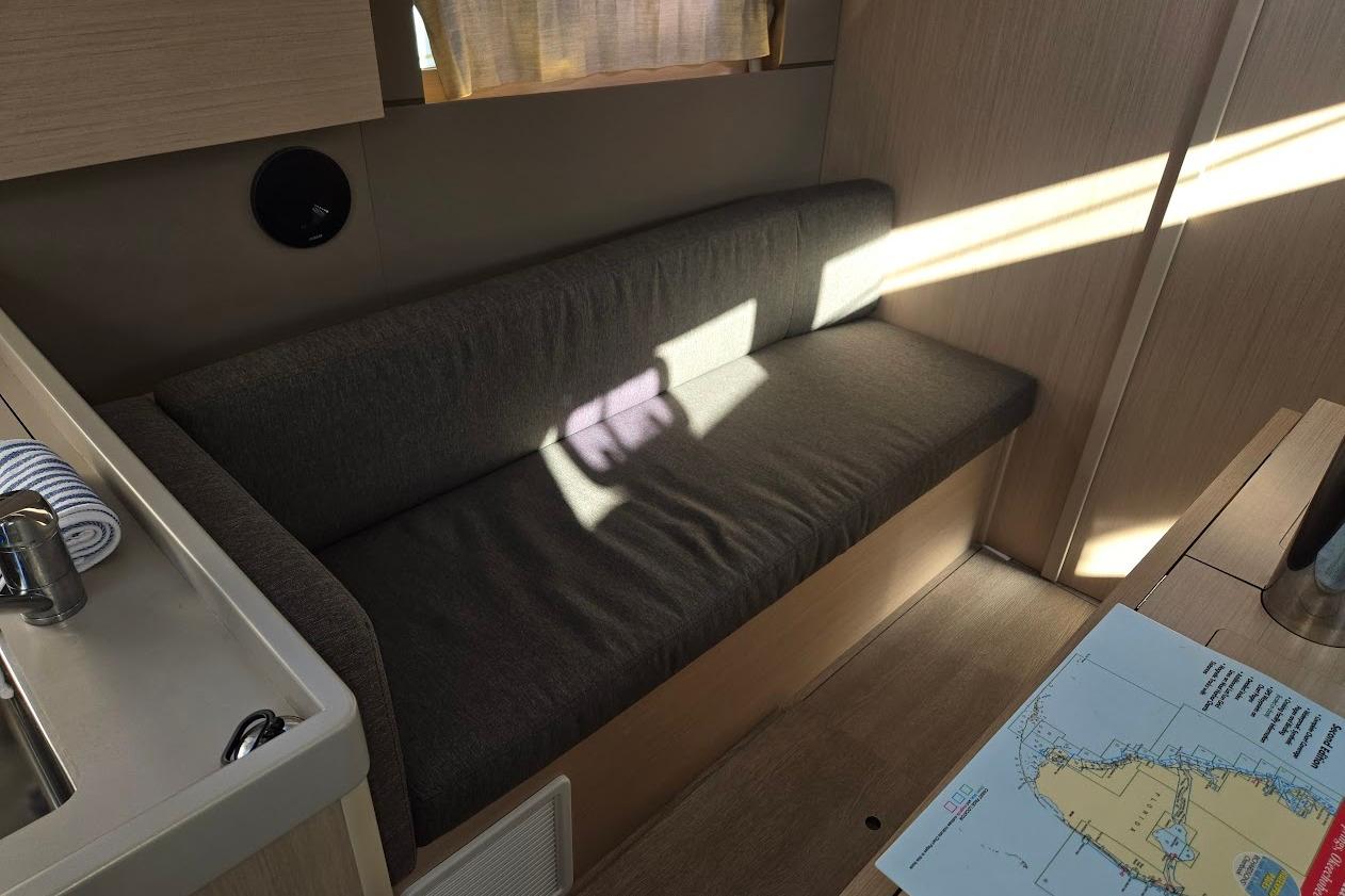 2023 Beneteau Oceanis 38.1 interior with sofa, map, and sunlight.