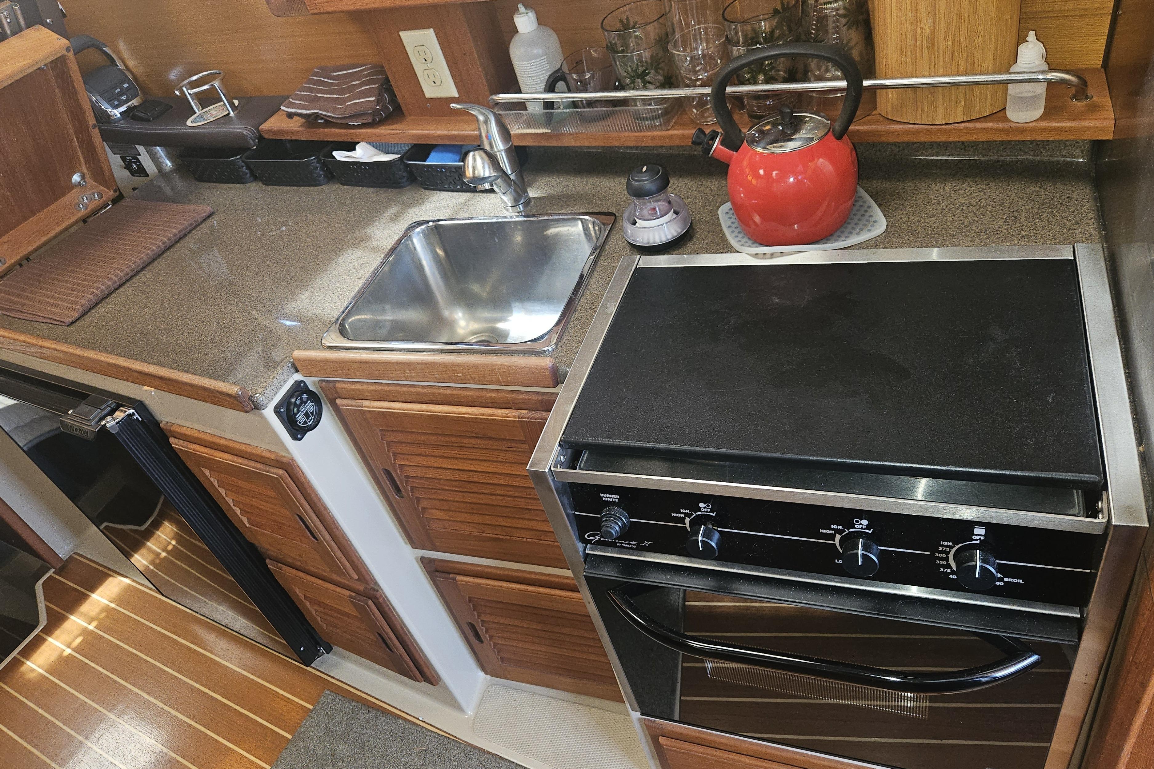 Compact kitchen in a 2014 Ranger Tugs R-27 boat with stove, sink, and red kettle.